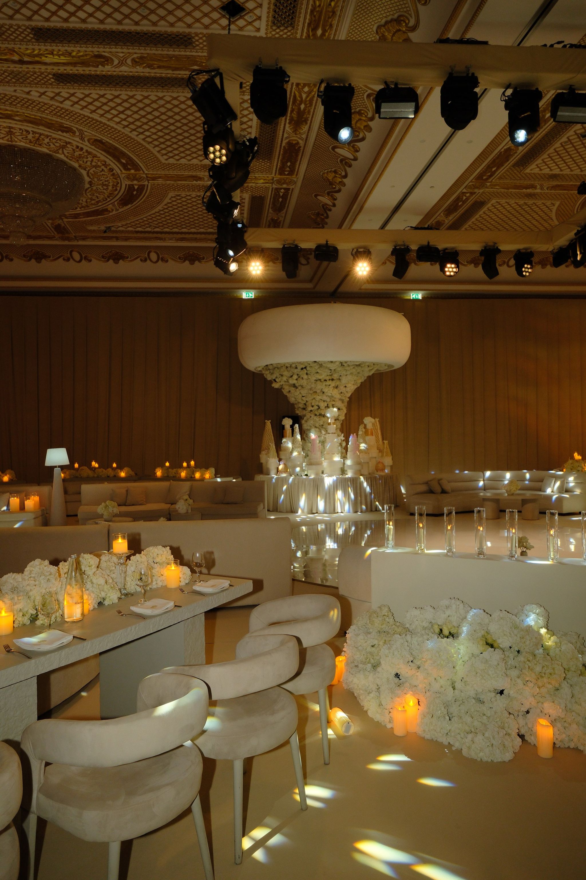 Ballroom dance floor washed with moving spotlights, framed by ivory lounge seating and floral tables