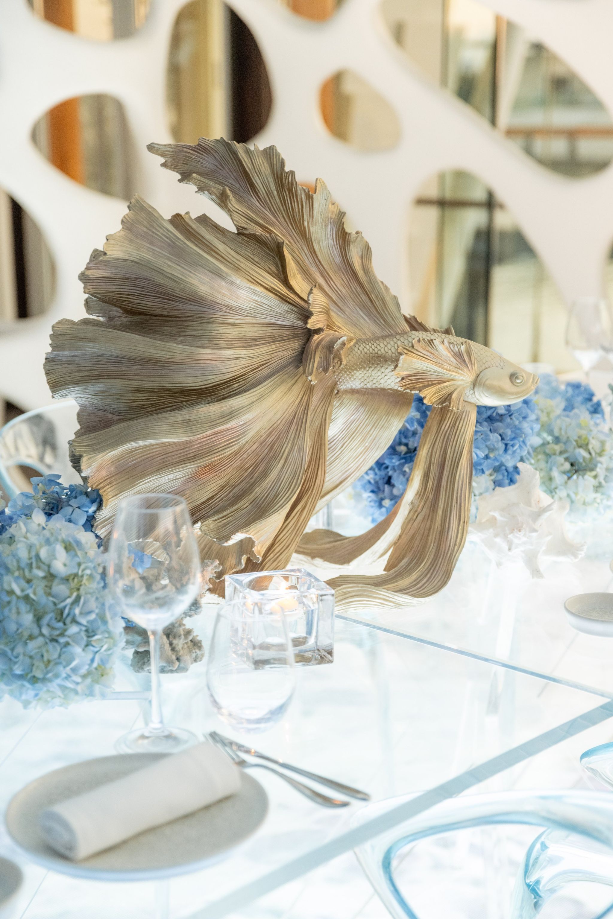 Close view of the gilded fish centrepiece above a place setting and blue hydrangeas
