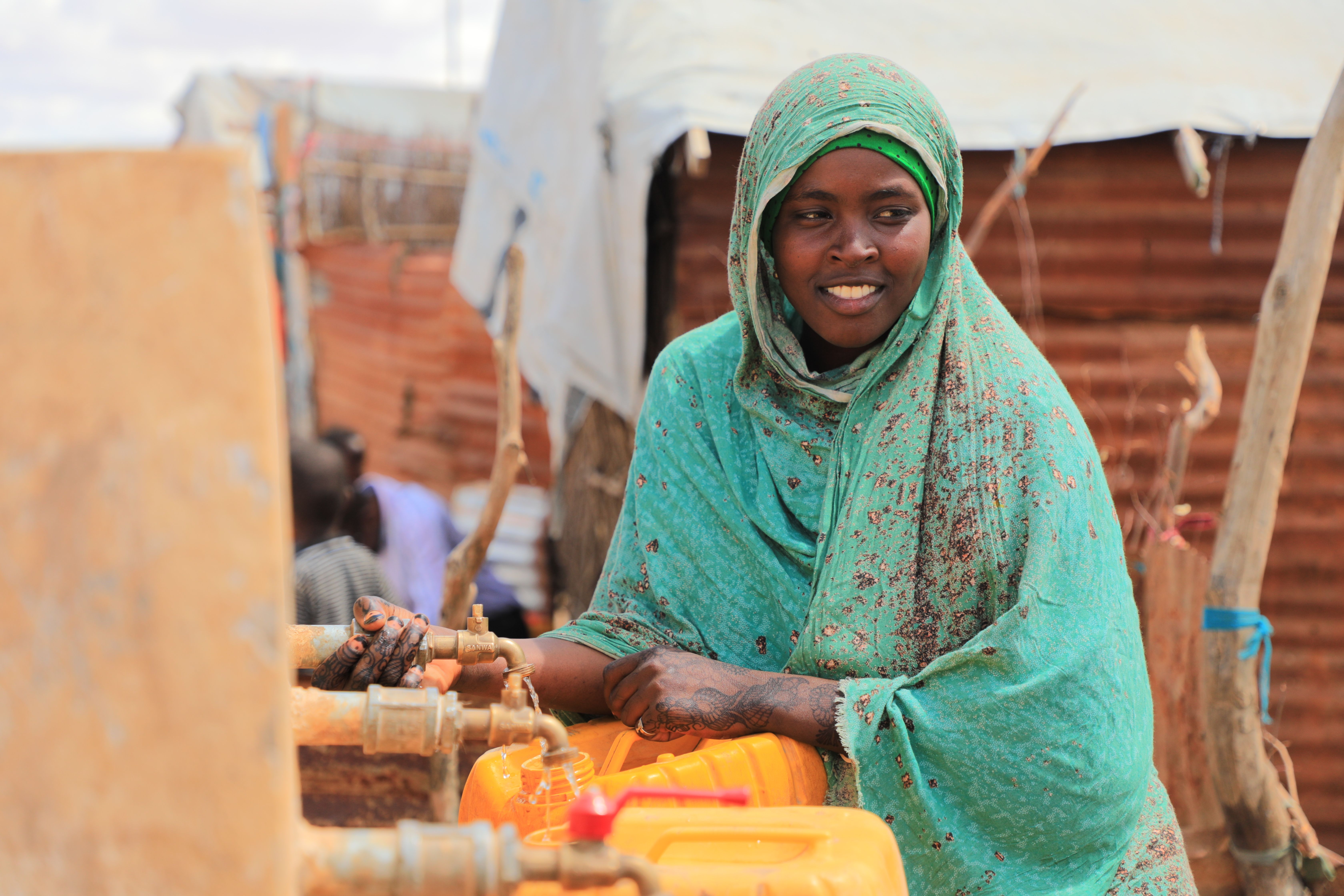 Aqiqah, a mother of three collects water from an Oxfam-constructed water tank