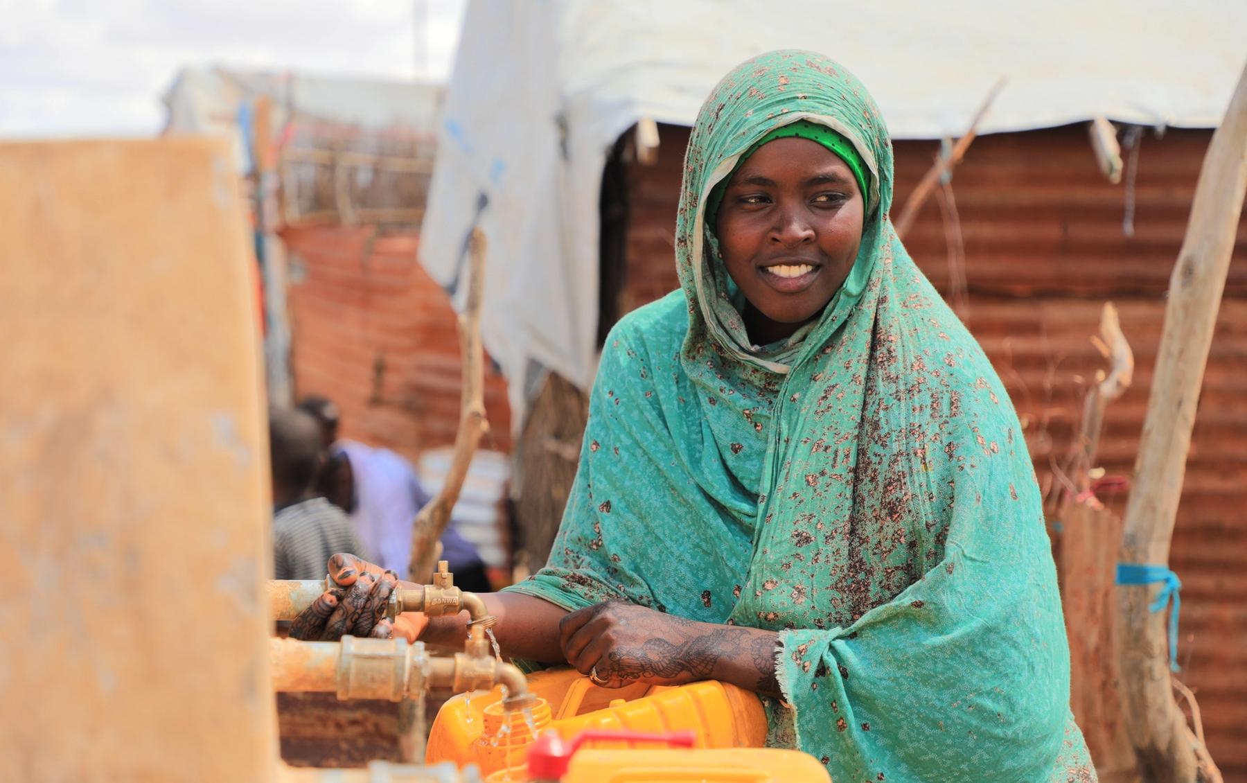 Aqiqah, a mother of three collects water from an Oxfam-constructed water tank