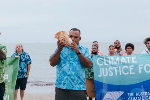 Traditional land owners and civil society blow conch shells on Fiji beach at Pre-COP