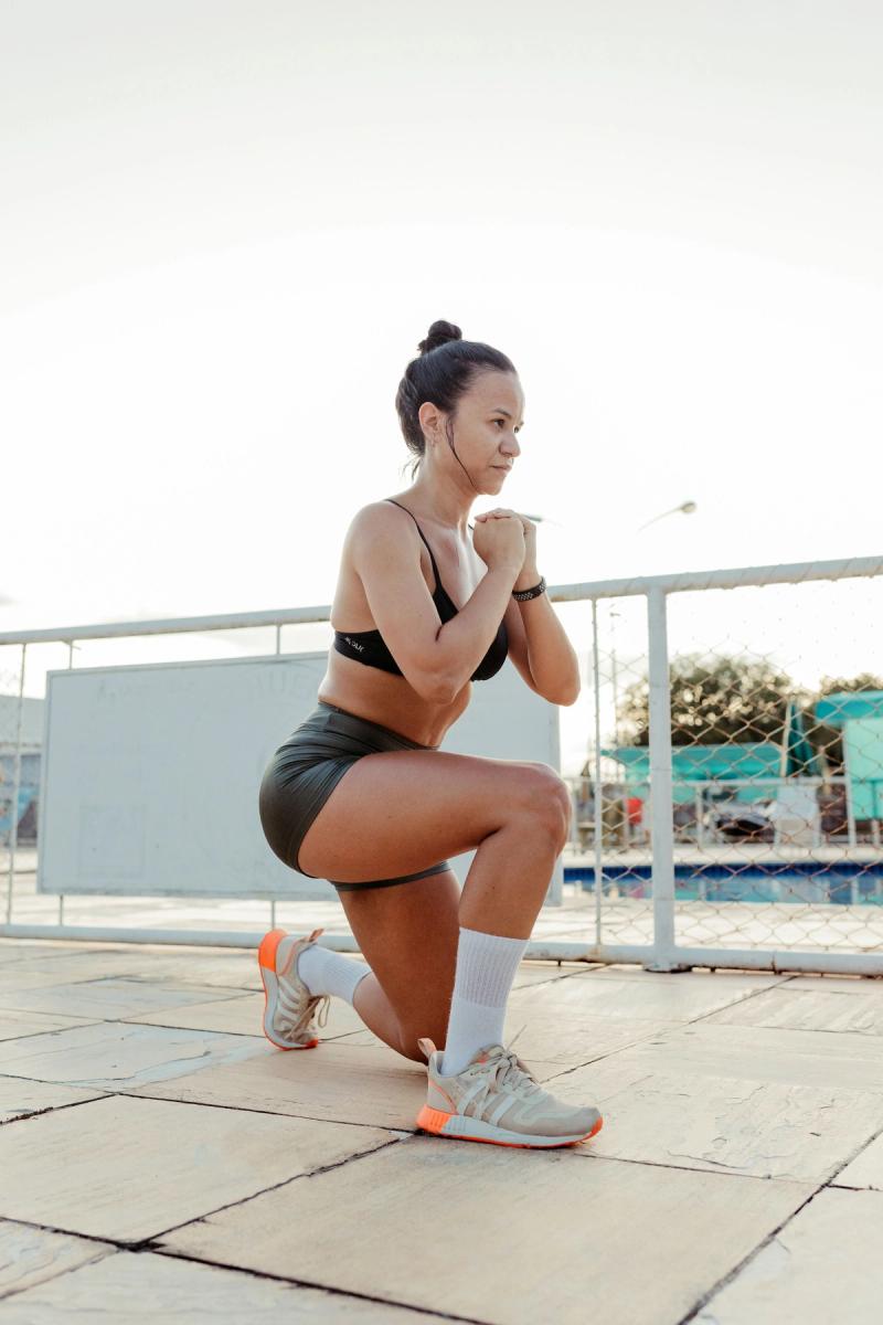 A woman holds the bottom of a lunge on a paved outdoor area near a pool.