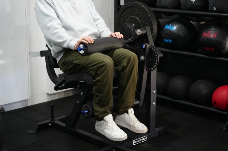 A man flexes his legs against the padded roller of the seated hamstring curl.