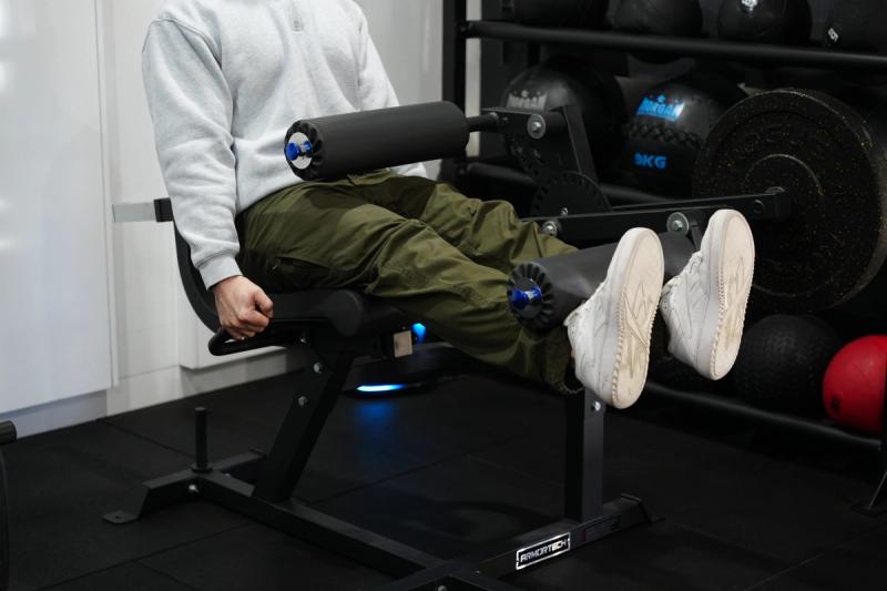 A man extends his legs against the padded roller of a seated leg extension machine in a gym.