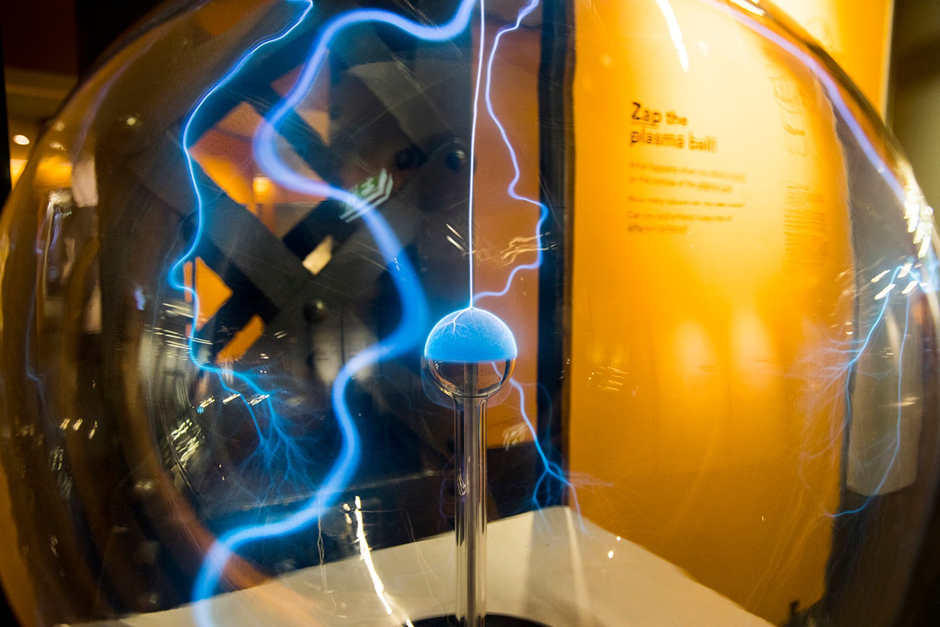 A plasma ball with blue squiggles inside a in glass case in front of an exhibition label