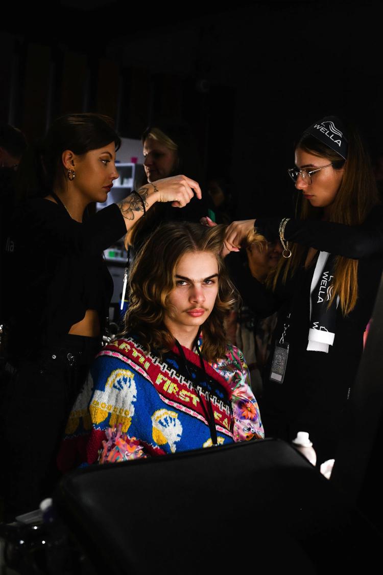 A model looks at the camera while getting their hair done backstage.