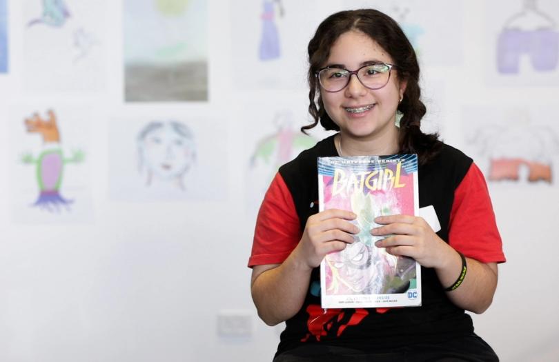 A Creative Studio participant wearing a black and red shirt holds up a ‘Bat Girl’ comic book