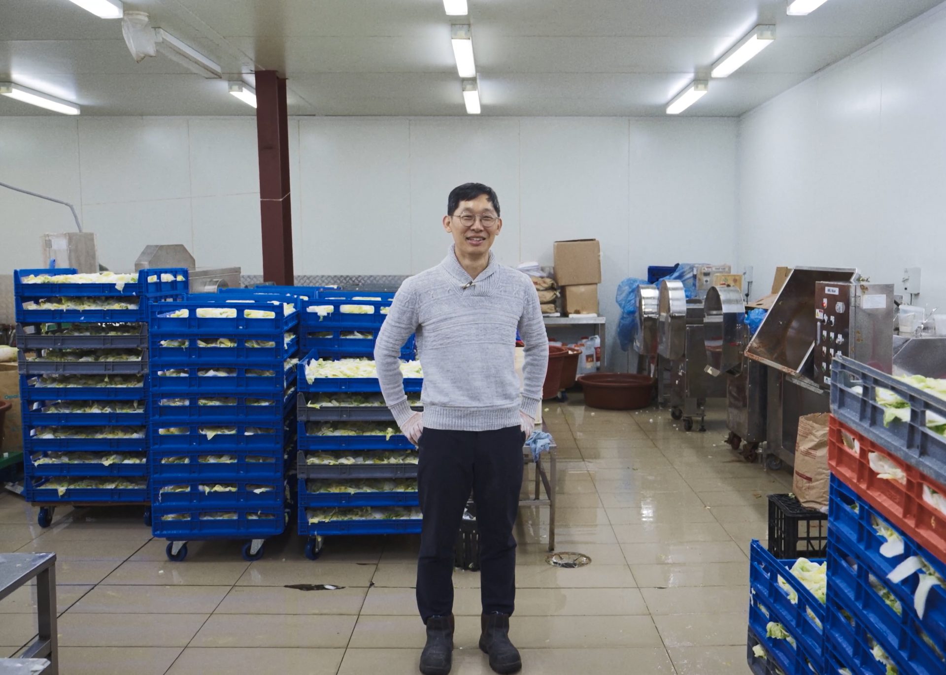 A man standing in an indoor manufacturing factory, with pallets of cabbage behind him.