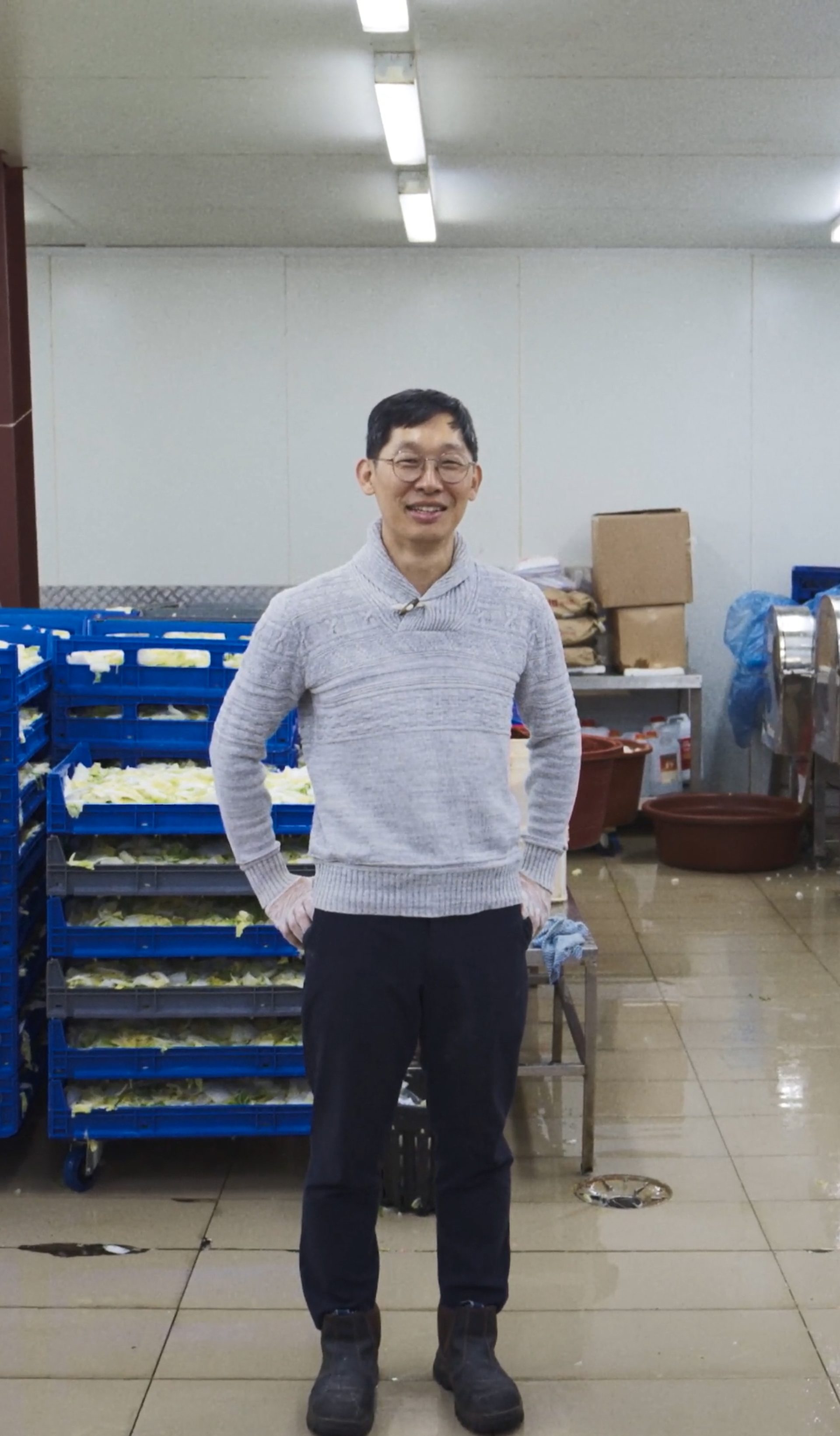 A man standing in an indoor manufacturing factory, with pallets of cabbage behind him.