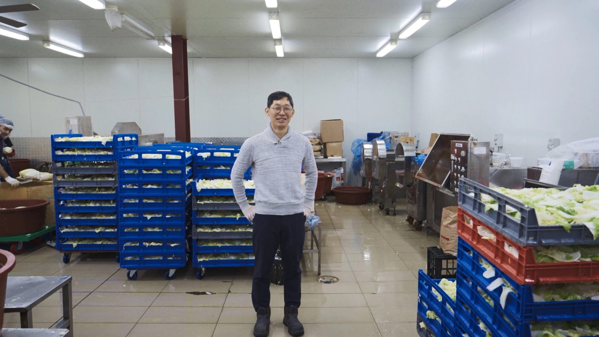 A man standing in an indoor manufacturing factory, with pallets of cabbage behind him.
