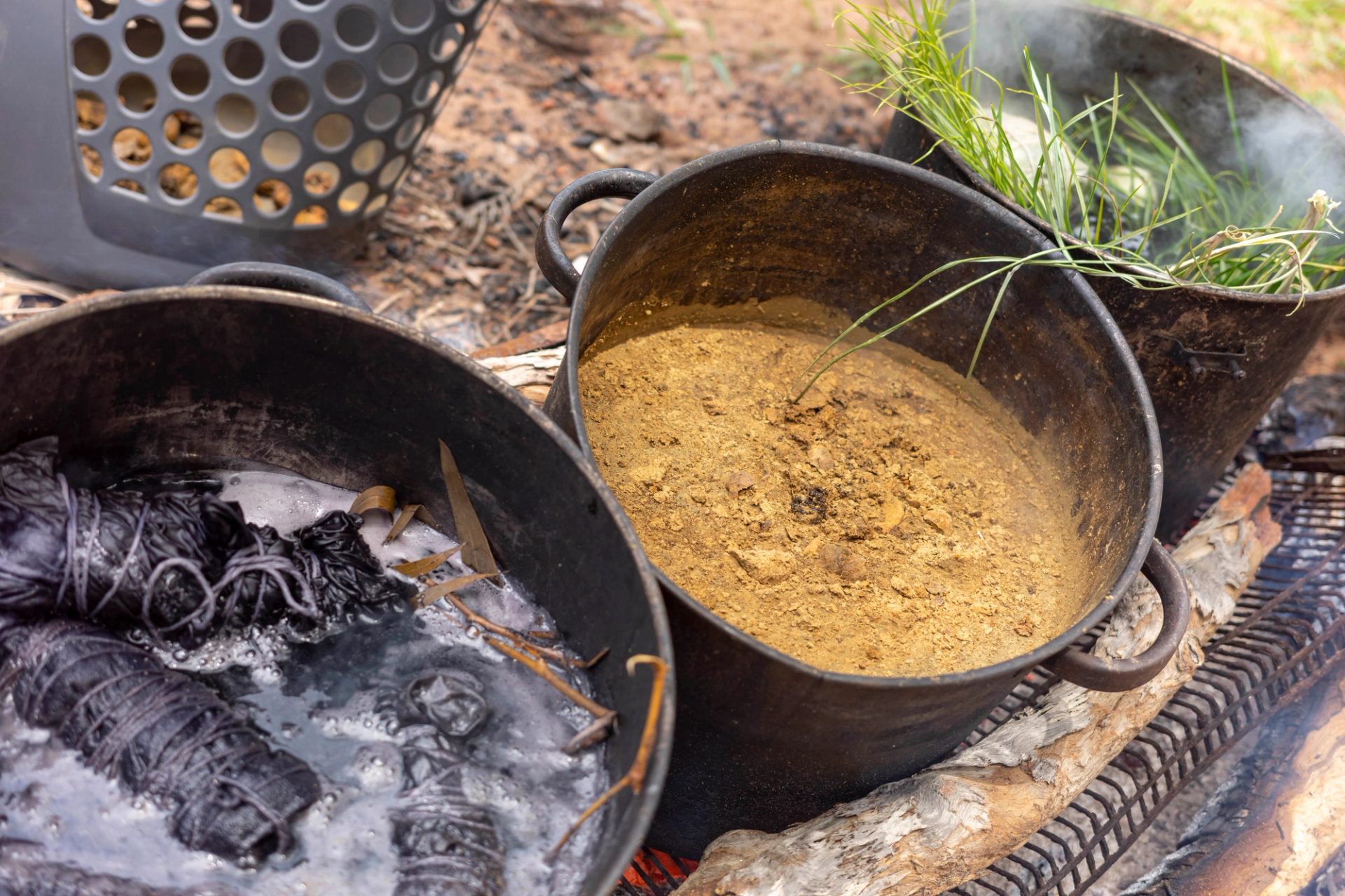 Three large pots boiling different plants to create coloured dyes.