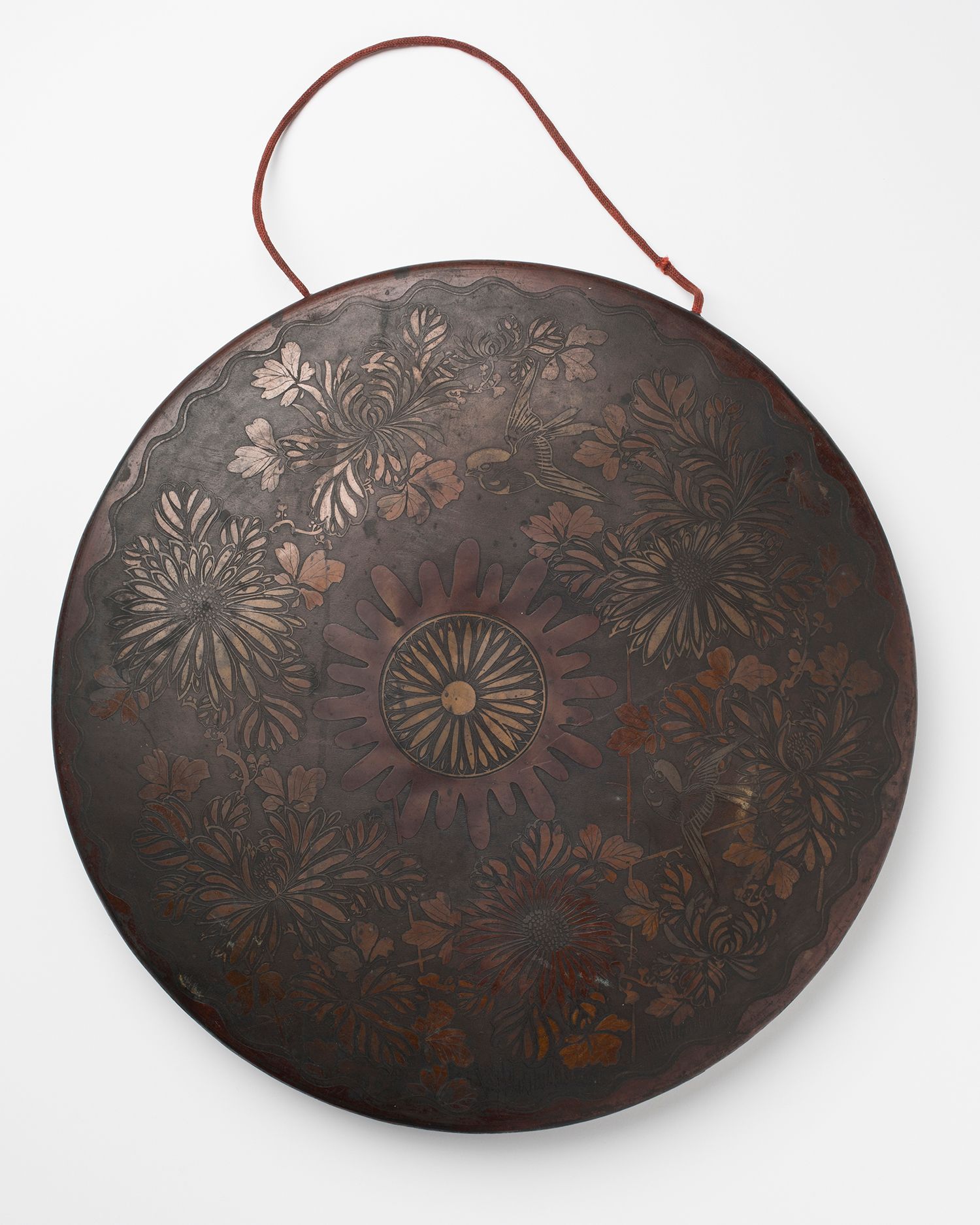 A brass circular gong with decorative flowers engraved onto the front surface.