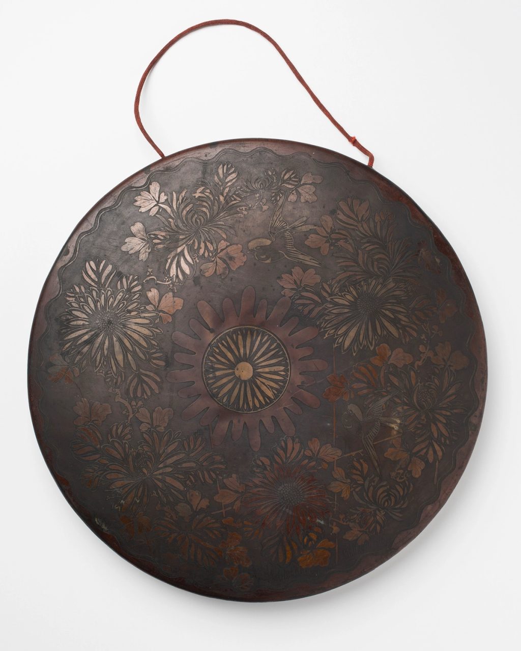 A brass circular gong with decorative flowers engraved onto the front surface.