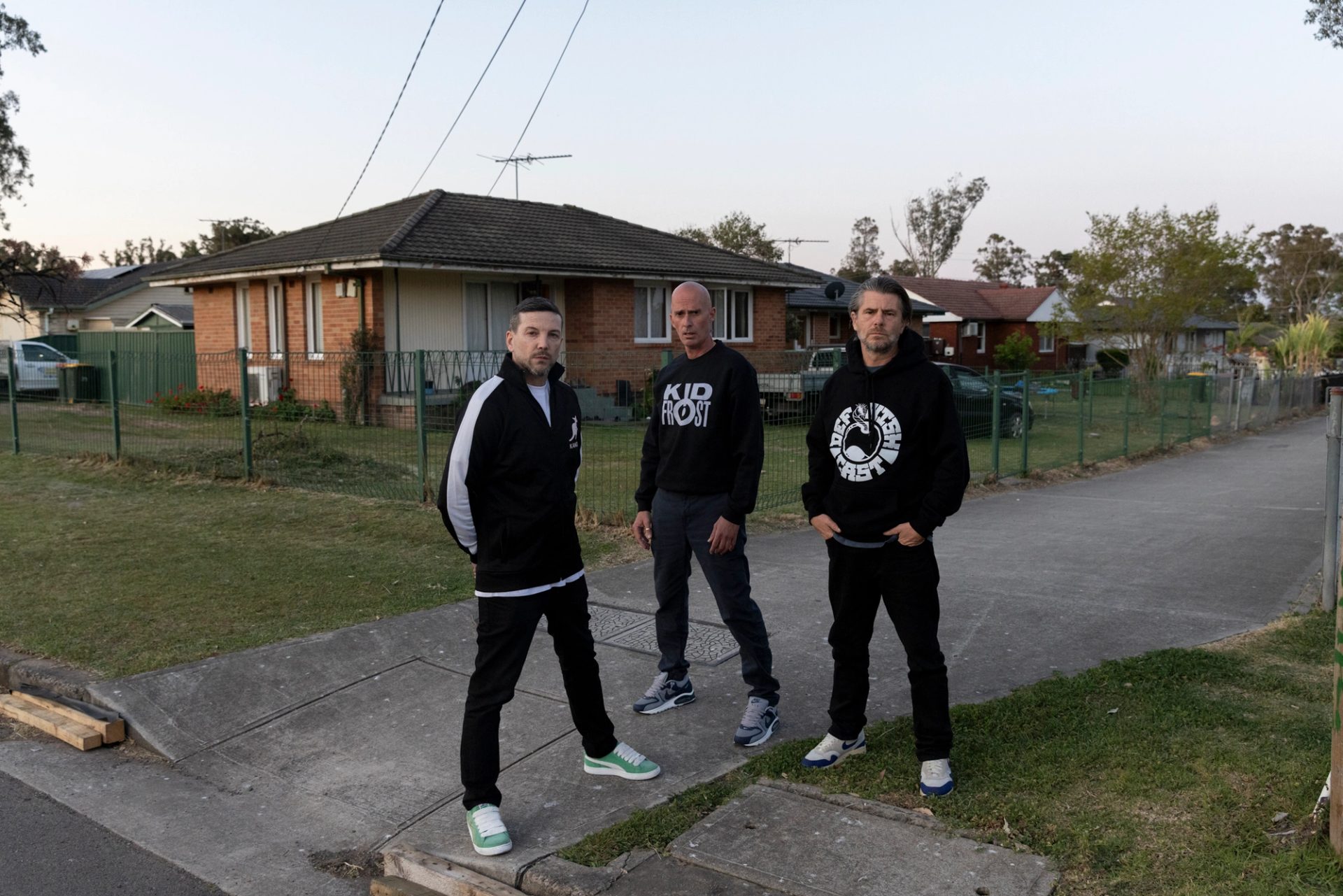 Three men standing on suburban street.