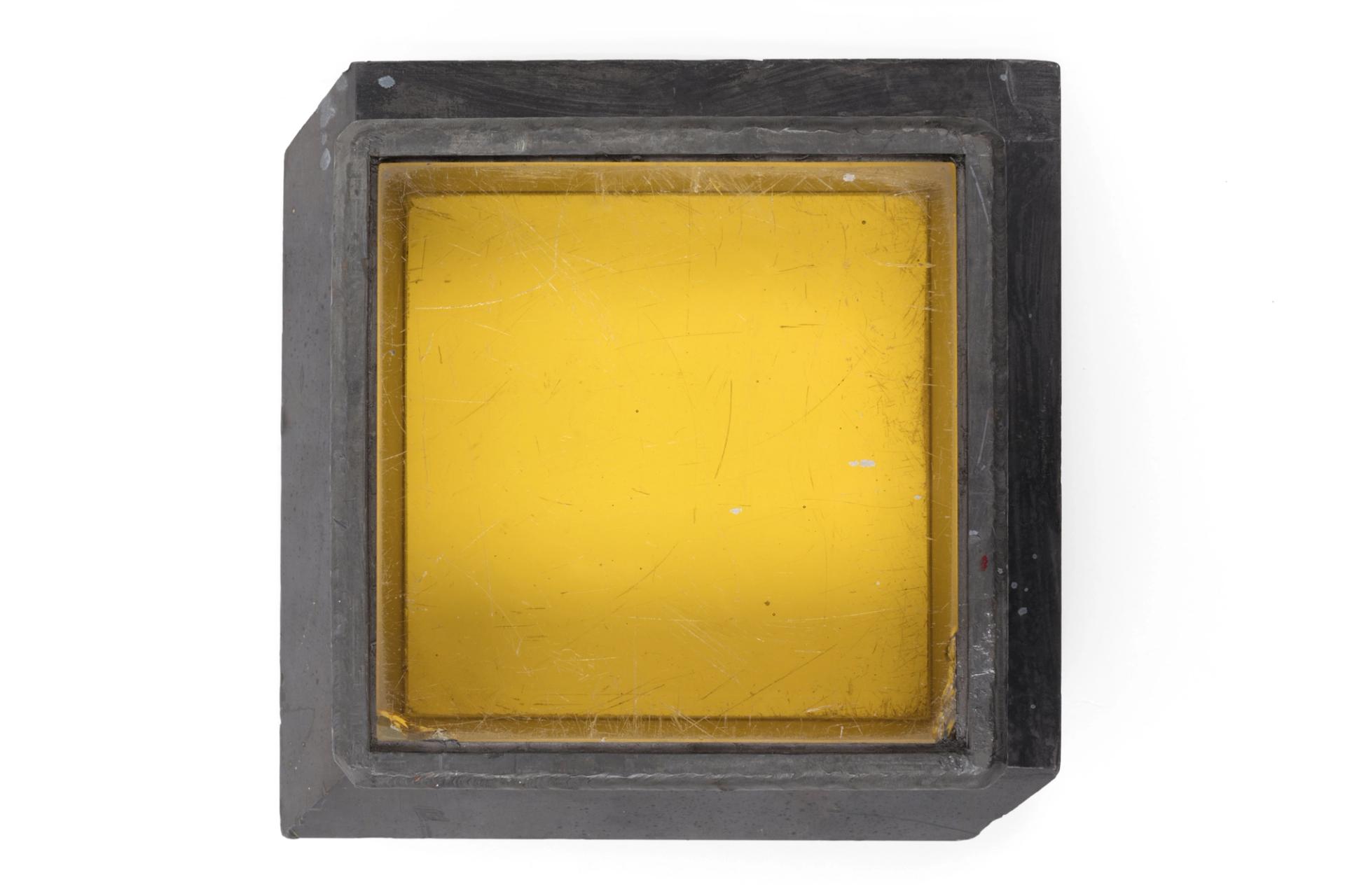 The thick glass has a yellow tinge from the presence of a small amount of cerium. Cerium is added to prevent the glass gradually turning brown from radiation damage. The glass is fitted within a grey lead frame.