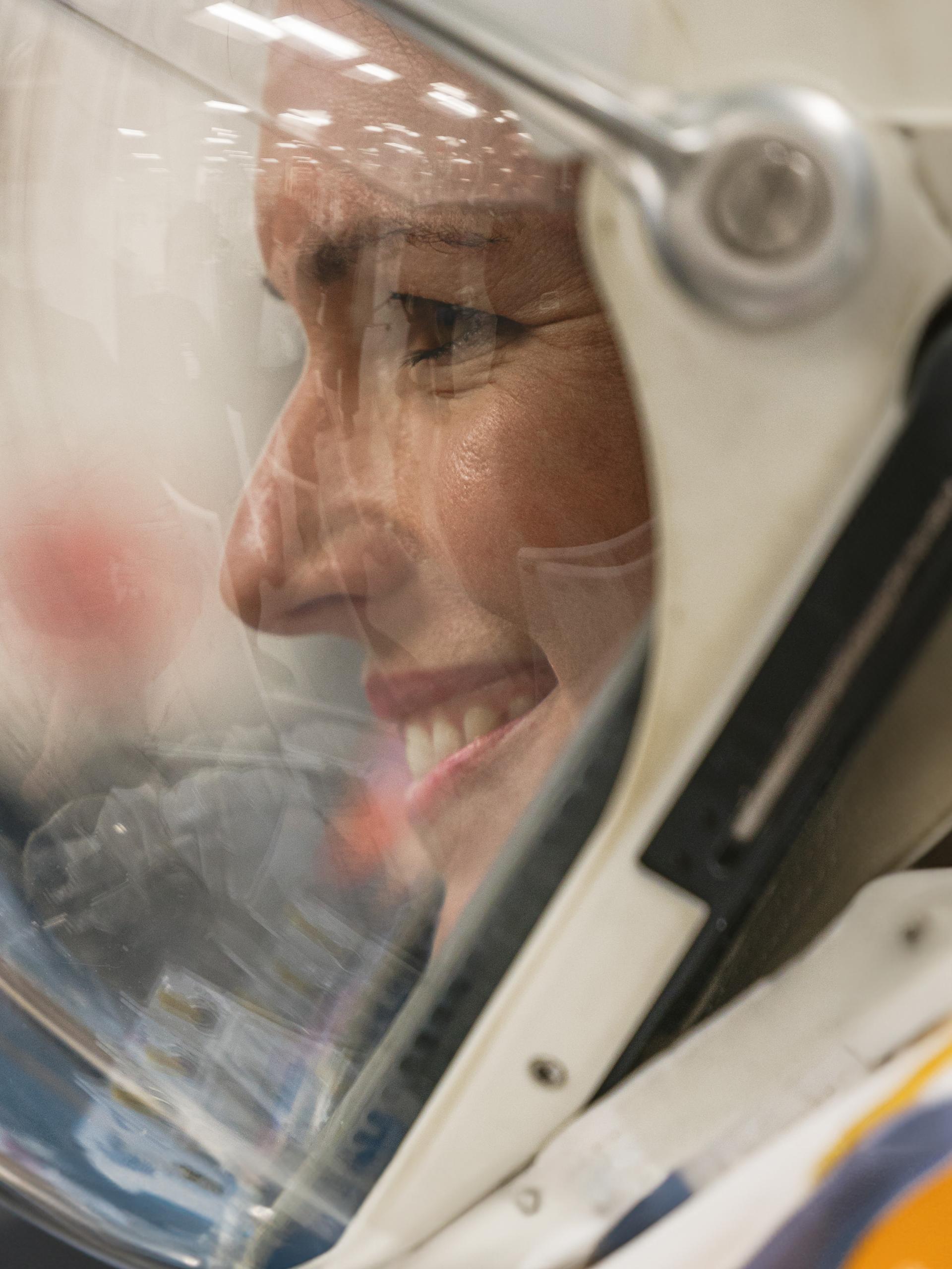 Side profile of woman in a space helmet, smiling.