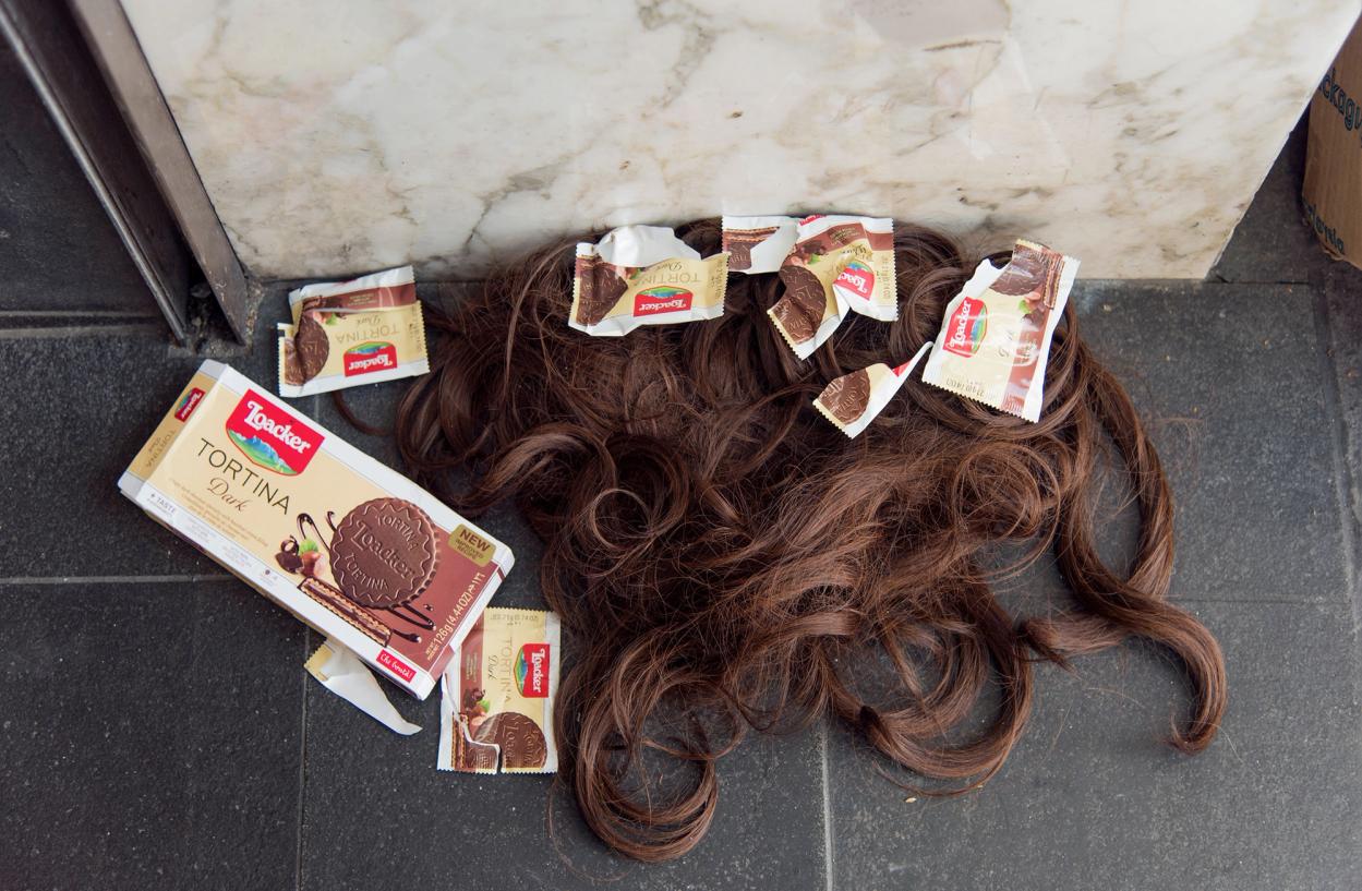 A brown wig lies on the ground with Tortina Dark wrappers.