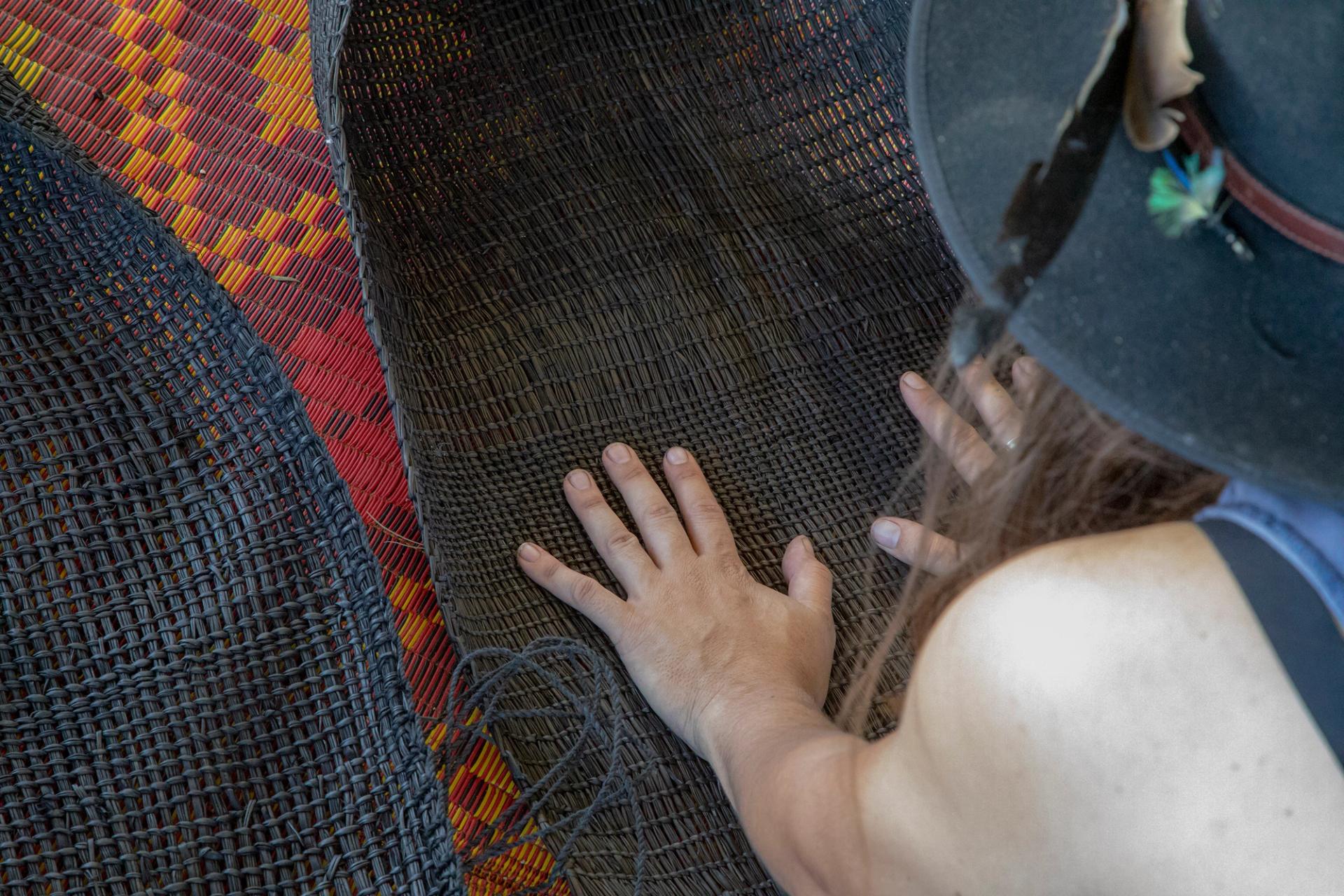 Two women’s hands on palm down on a black, flat woven surface.
