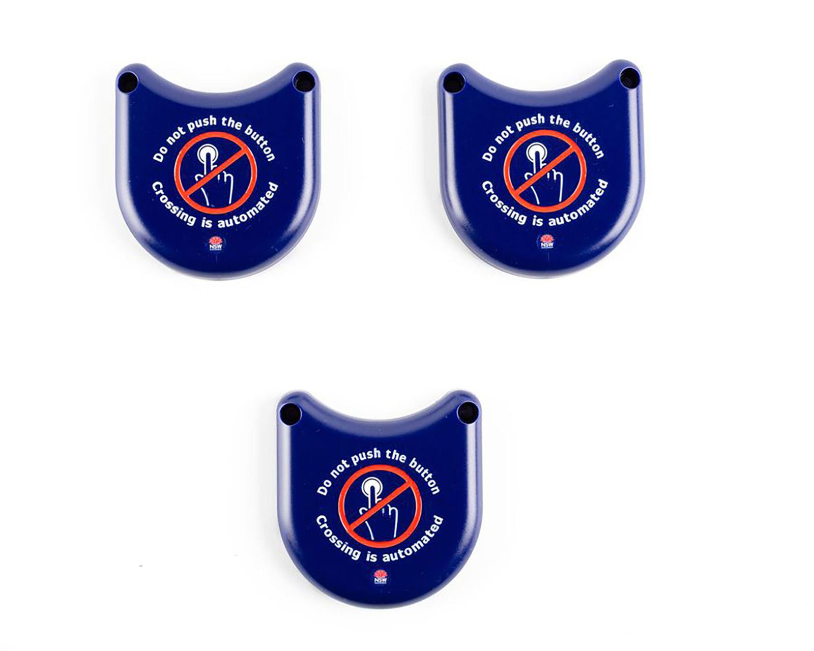 3 Solid plastic covers in dark blue. It has a curved design that can slot over the bottom half of the pedestrian traffic light buttons. It is designed to prevent people from touching the buttons surface as a safety measure due to the COVID-19 pandemic. Messaging on the button is designed to let pedestrians know not to touch surfaces as crossing have been automated. In the centre of the button is a graphic of a crossed out hand pushing a button to support text visually. It utilises the "do-not-do" graphic of a red circle with diagonal line through it.