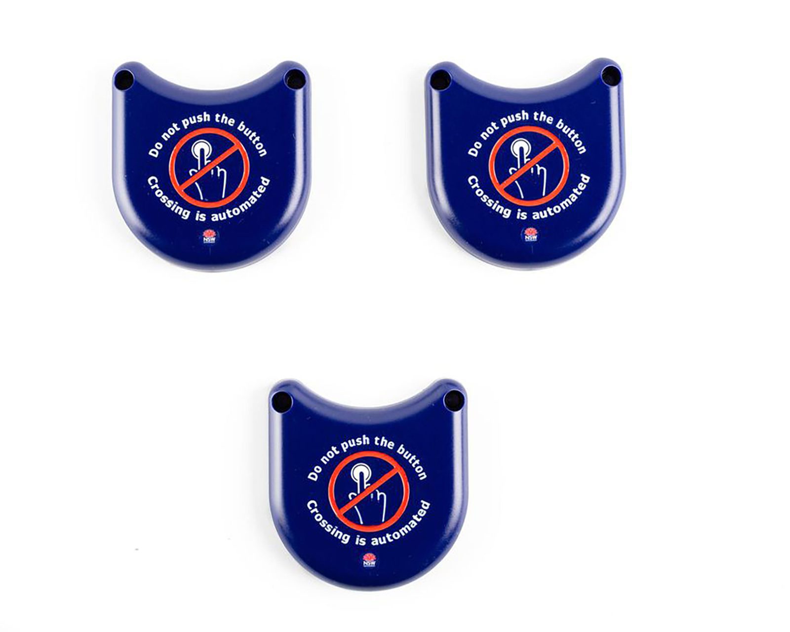 3 Solid plastic covers in dark blue. It has a curved design that can slot over the bottom half of the pedestrian traffic light buttons. It is designed to prevent people from touching the buttons surface as a safety measure due to the COVID-19 pandemic. Messaging on the button is designed to let pedestrians know not to touch surfaces as crossing have been automated. In the centre of the button is a graphic of a crossed out hand pushing a button to support text visually. It utilises the "do-not-do" graphic of a red circle with diagonal line through it.