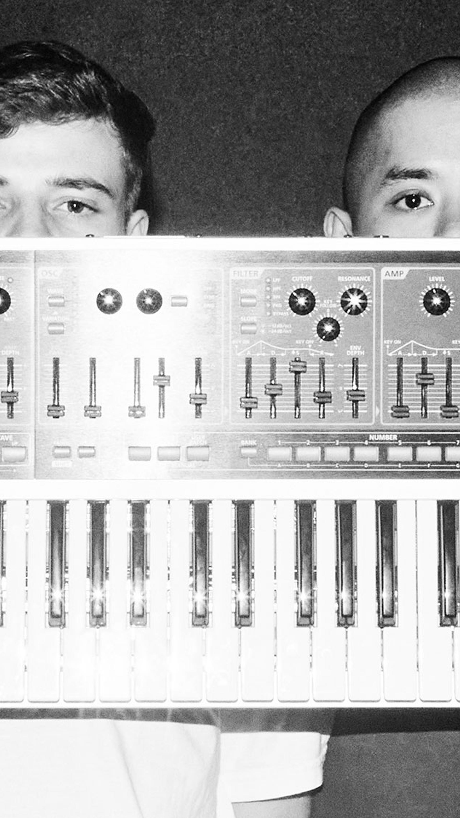 Two fellas hold a single keyboard synth in front of their faces