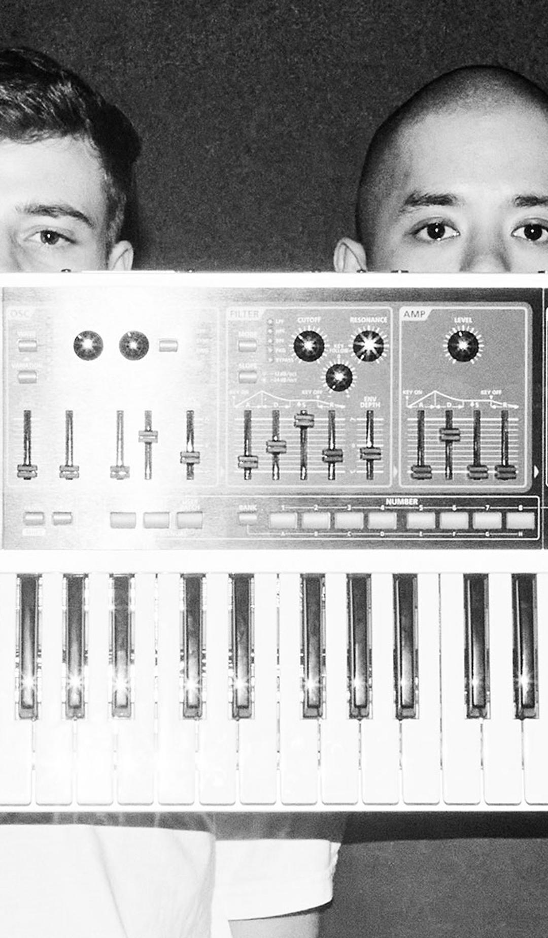 Two fellas hold a single keyboard synth in front of their faces
