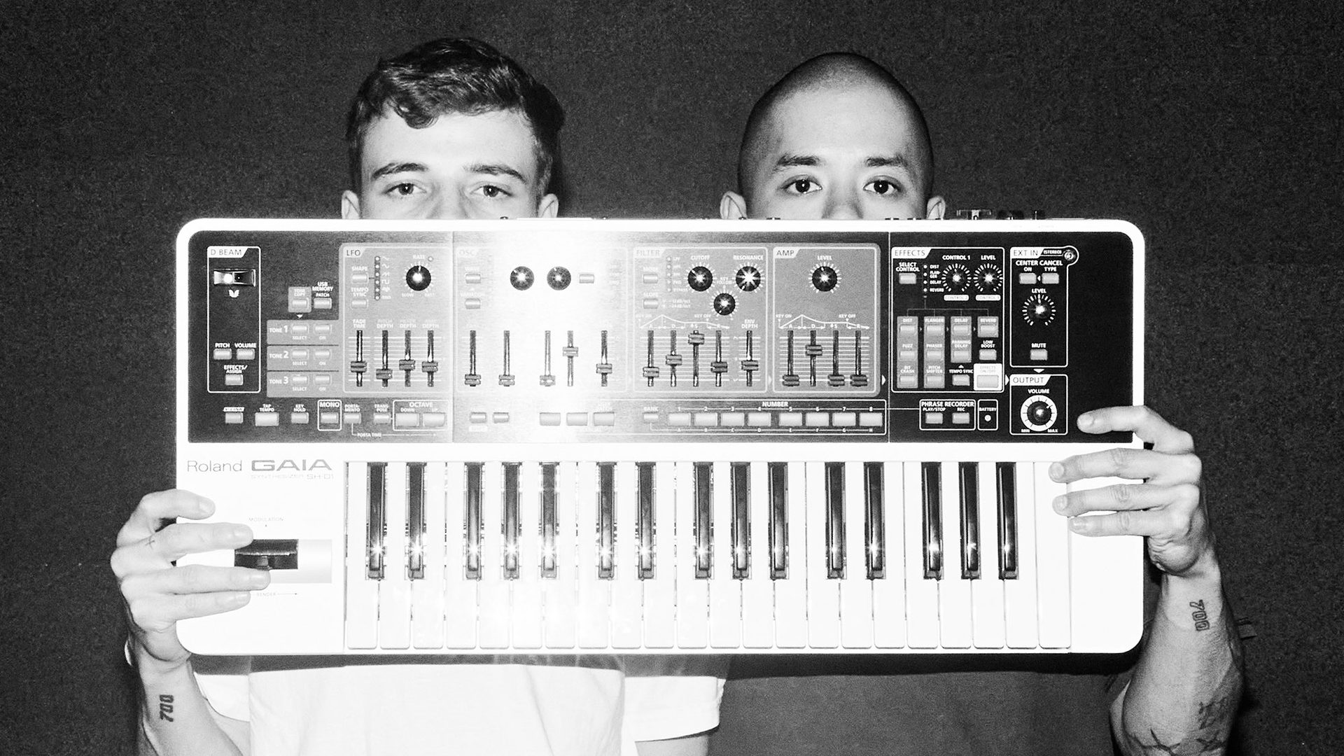 Two fellas hold a single keyboard synth in front of their faces