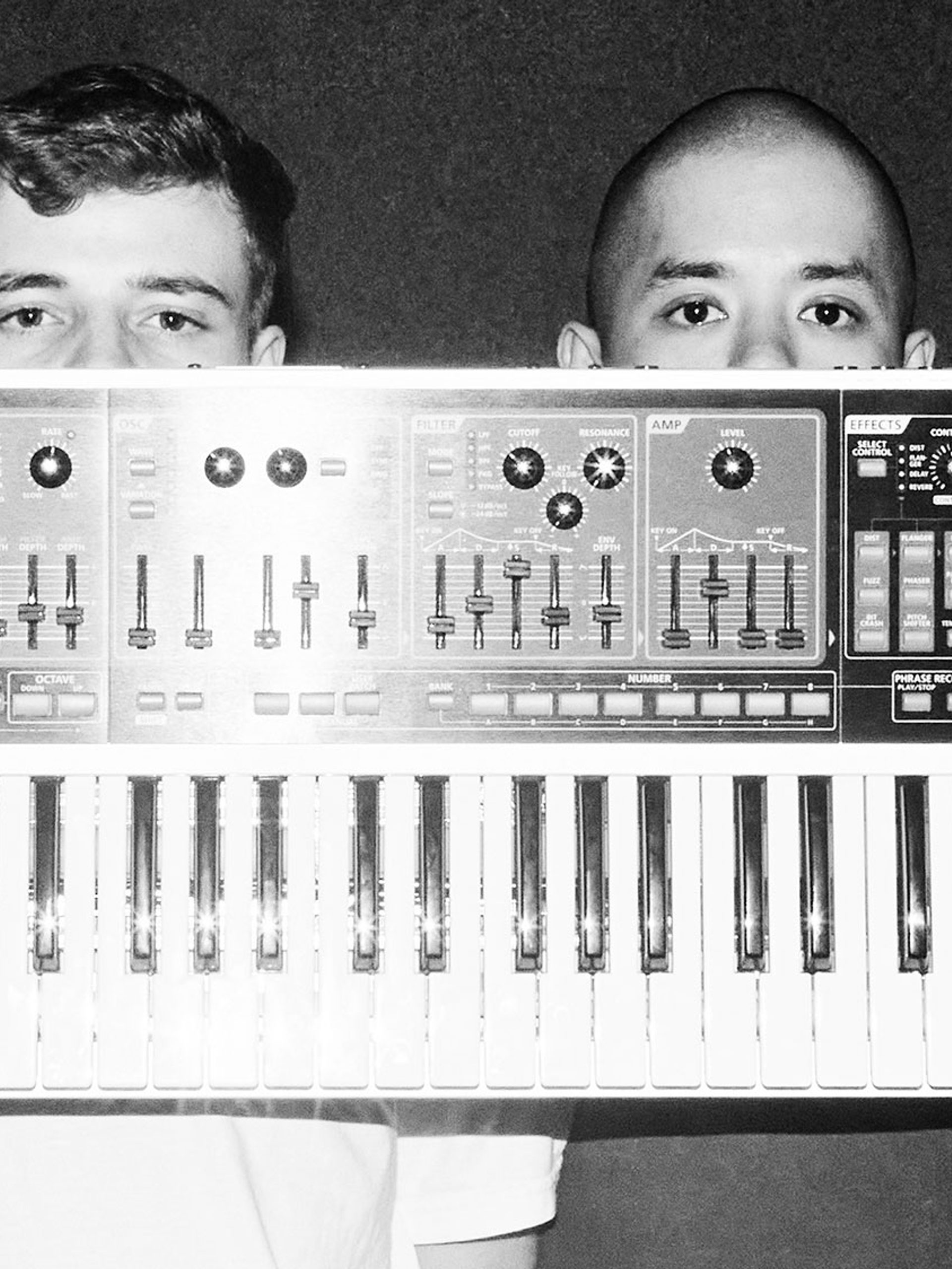 Two fellas hold a single keyboard synth in front of their faces