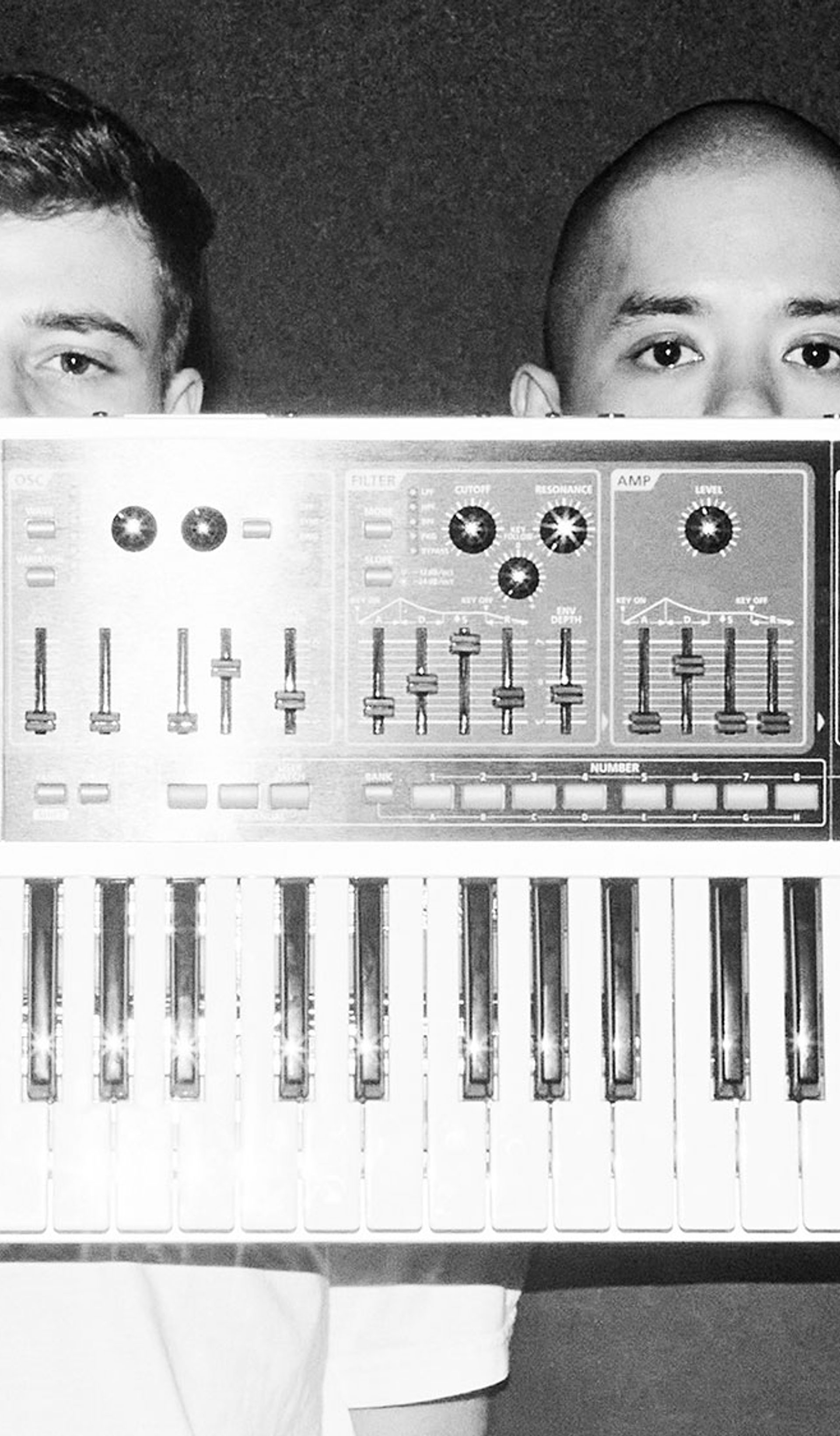 Two fellas hold a single keyboard synth in front of their faces