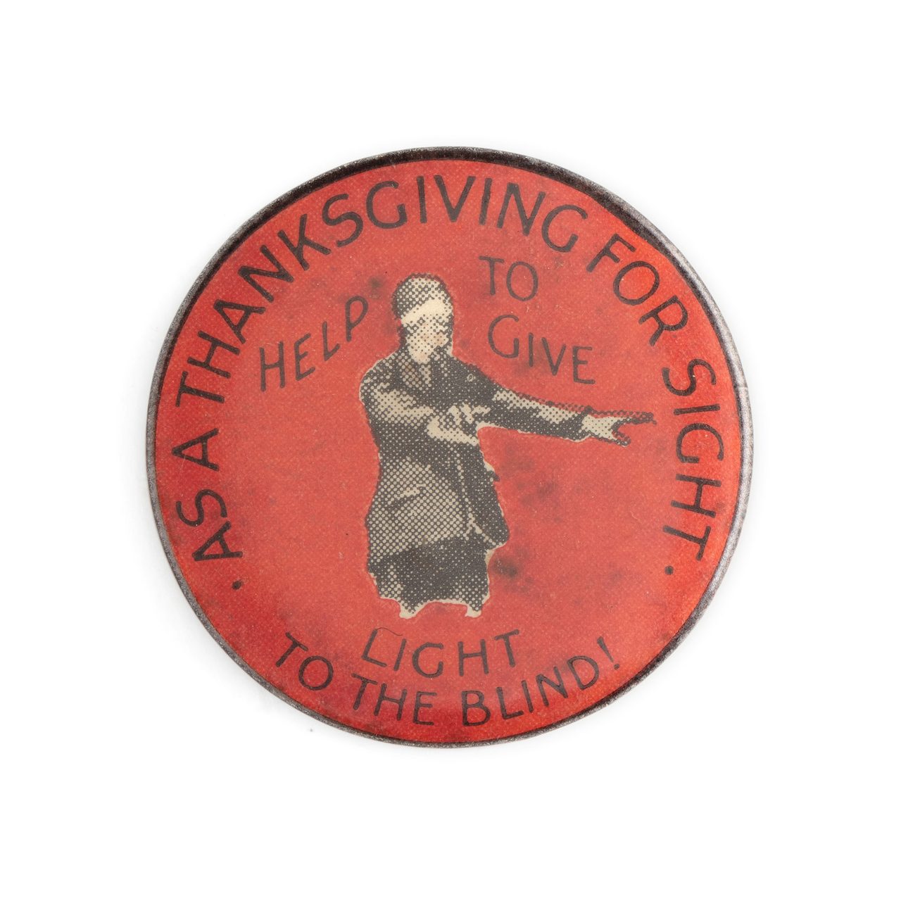Red circular badge with monochrome image of man wearing blindfold with arms outstretched. Text in black: AS A THANKSGIVING FOR SIGHT HELP TO GIVE LIGHT TO THE BLIND. Text in red along black edge: A W PATRICK MAKER 440 RAE ST N FITZROY MELBNE.
