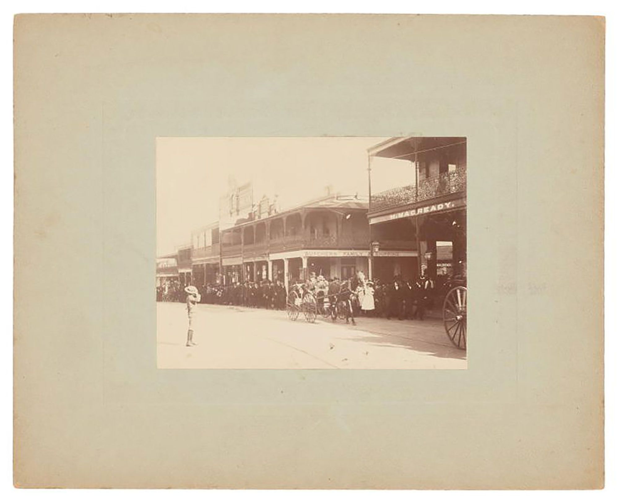 Mounted black and white photograph depicting a girl seated in a long sleeve, full-length dress with foliage on her lap and around her feet.