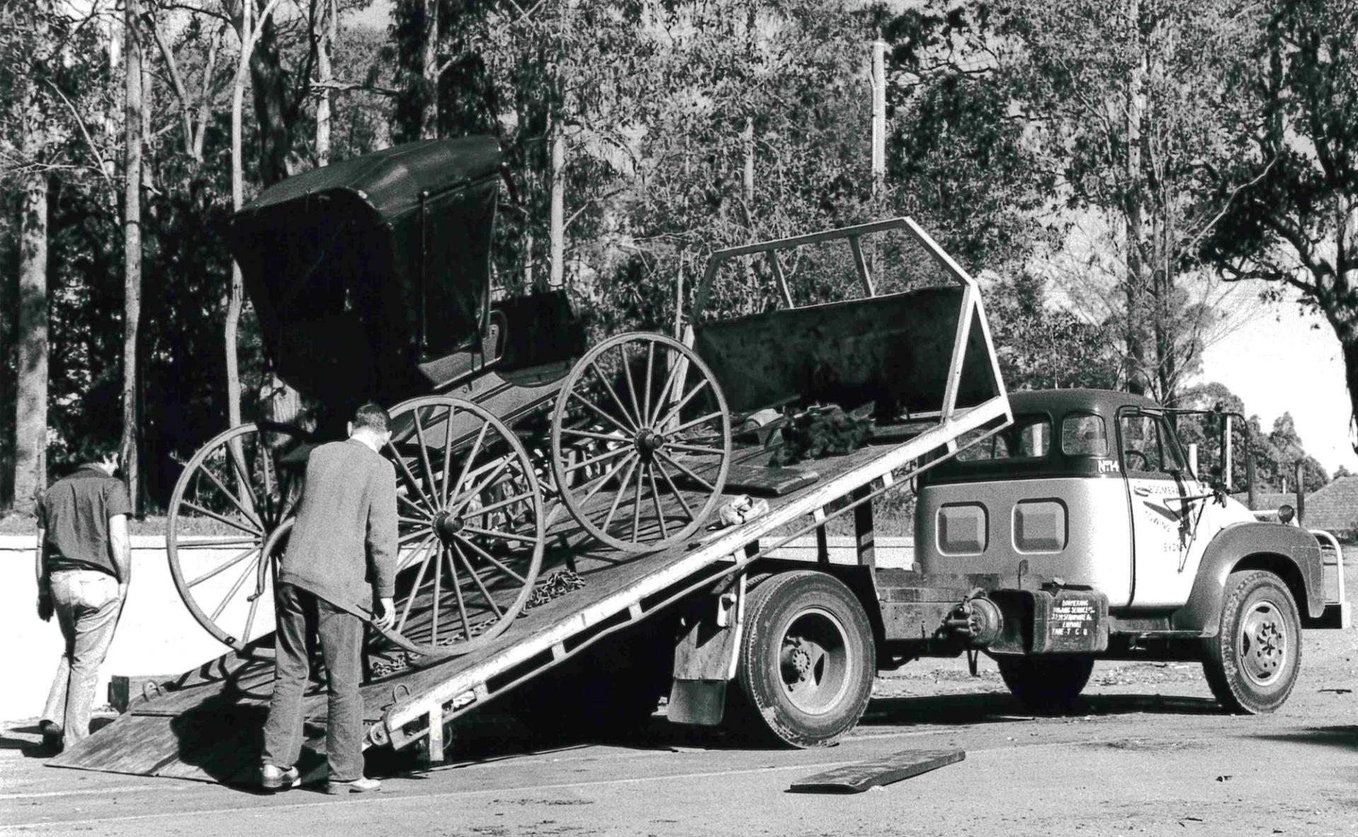Black and white image of a buggy being unloaded off a flat bed