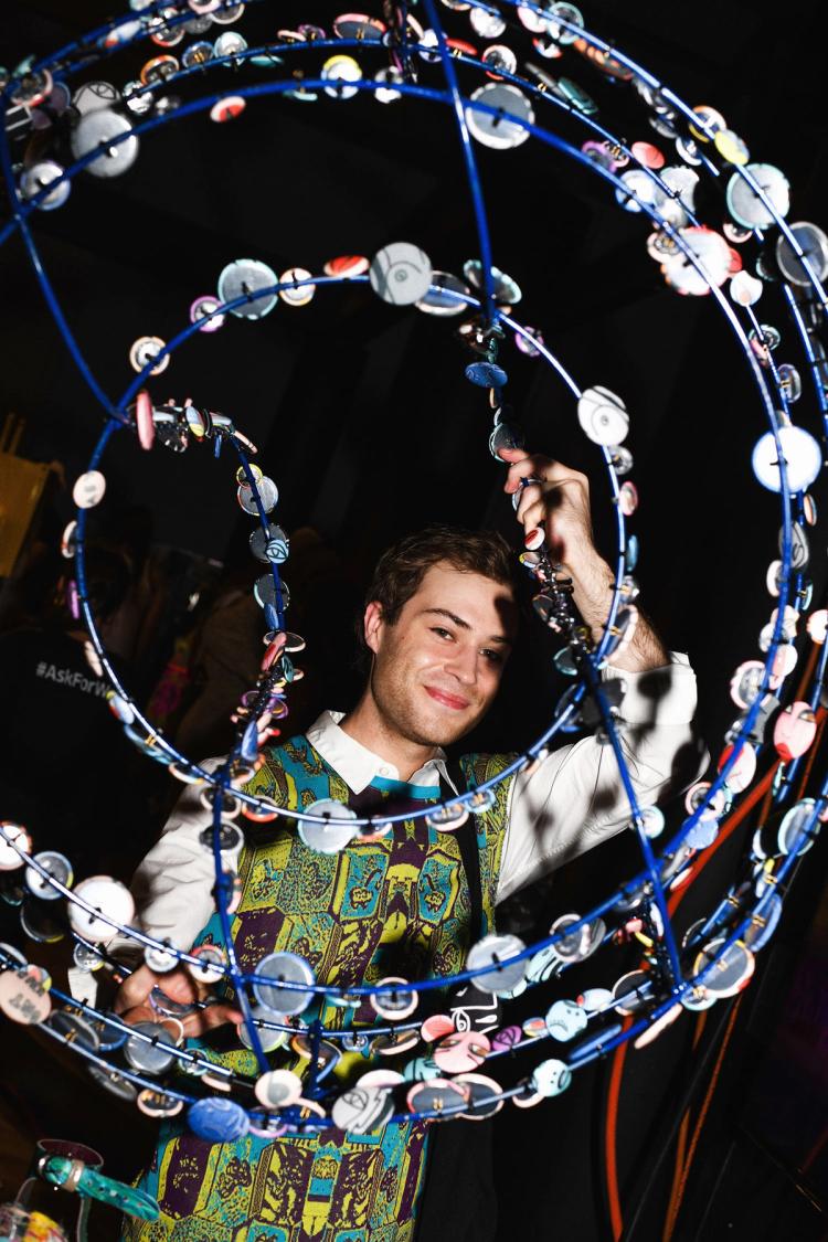 Max Rixon smiles while holding a wire frame adorned with buttons.