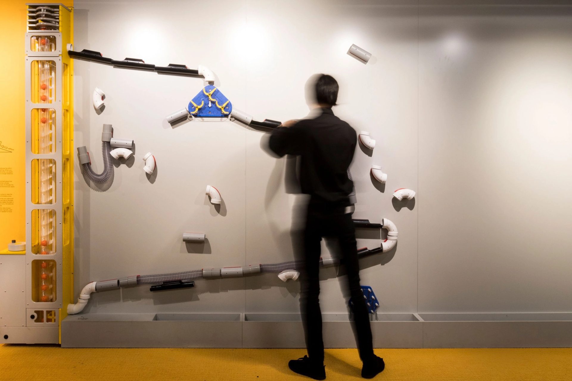 A man wearing all black is standing in front of a science based installation.