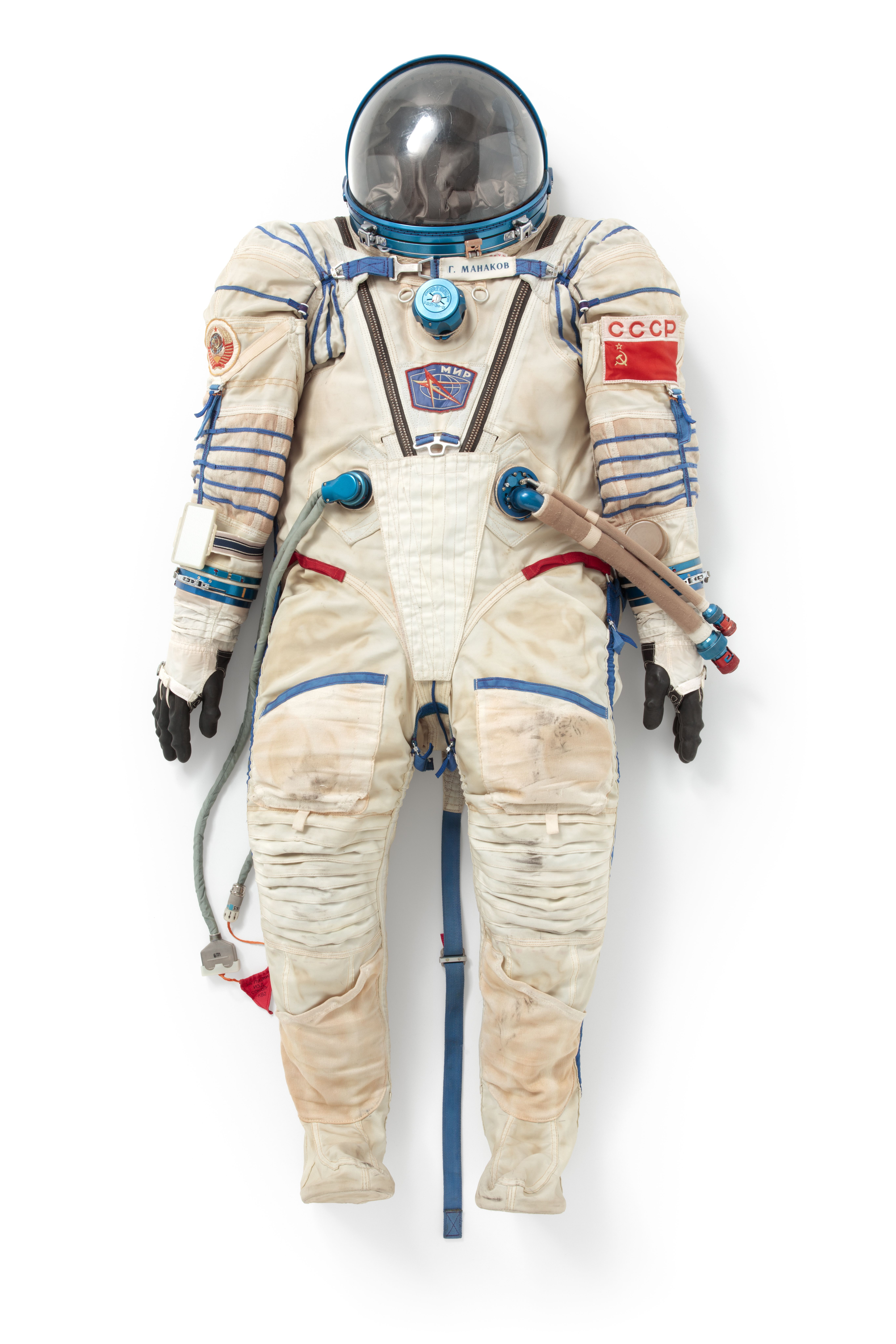 Sokol KV-2 spacesuit, consisting of pressure garment with hood, radio headset and canvas booties. The pressure garment is made of white nylon canvas, with a rubberised cloth lining. It has an attached pressurised hood, in place of a helmet, with a hinged plastic visor which secures to an anodised aluminium neck ring. Decorated with royal blue trim and appliqued patches.