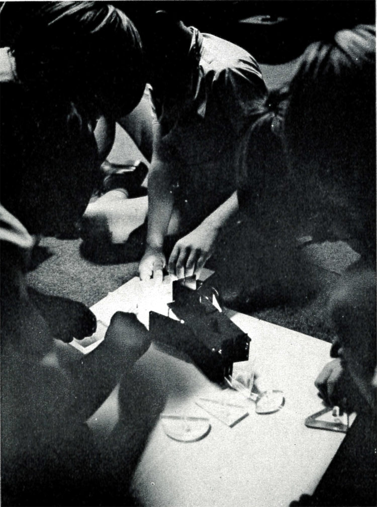 Black and white photograph of children hovering around small educational model