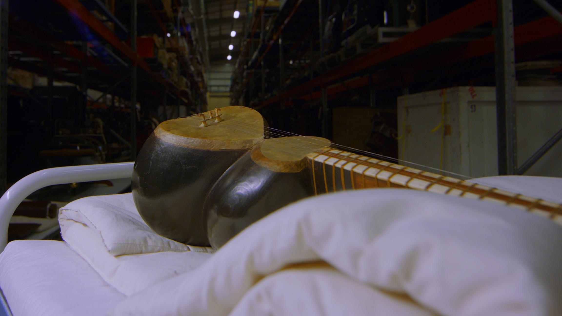 A close-up of the Persian tar musical instrument sitting on a trolley in a storeroom.