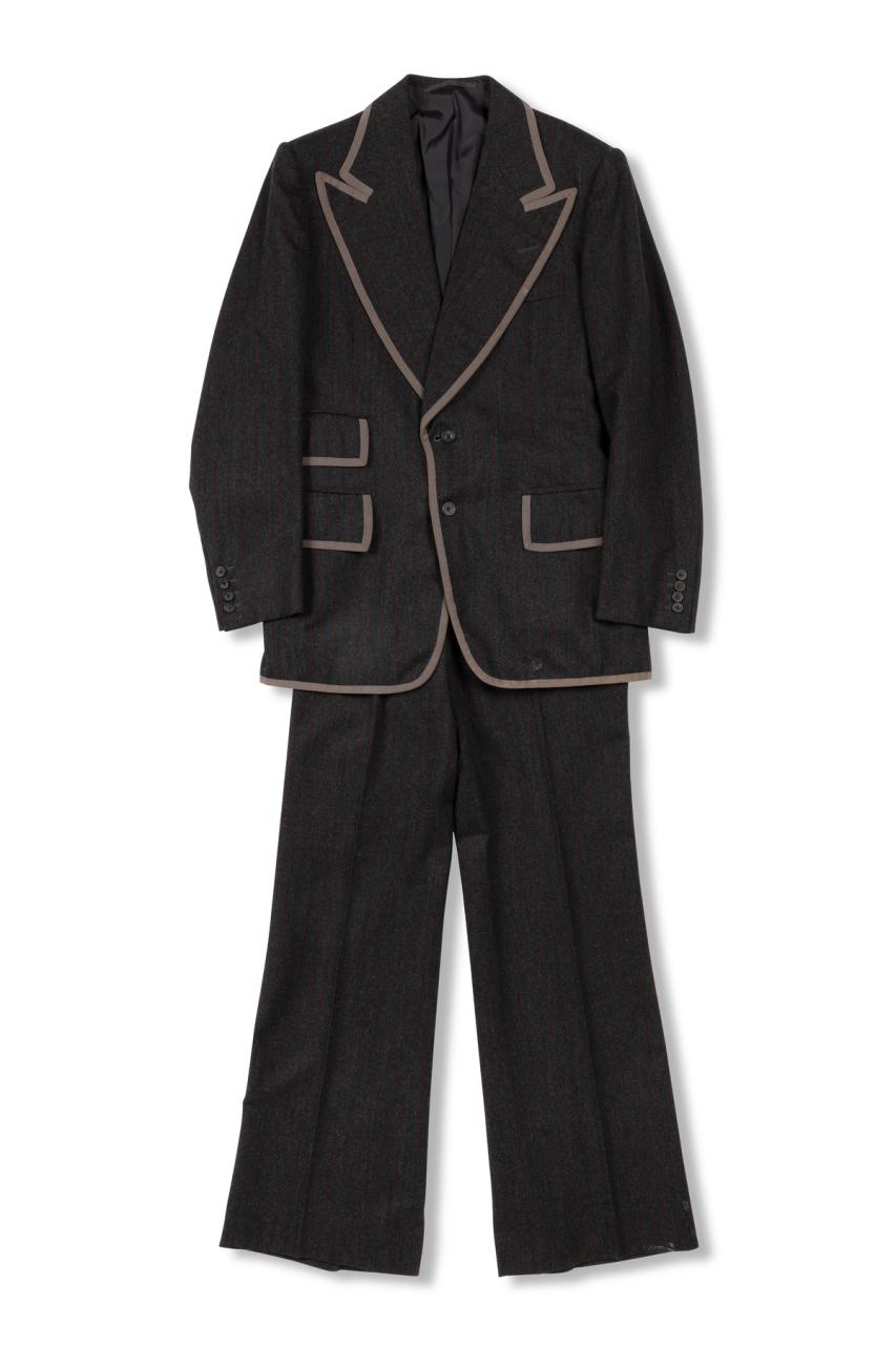 A dark brown mens suit of a blazer jacket and trousers made with wool and silk, the brim of the collar, pockets and sleeves are lined with a light brown fabric.