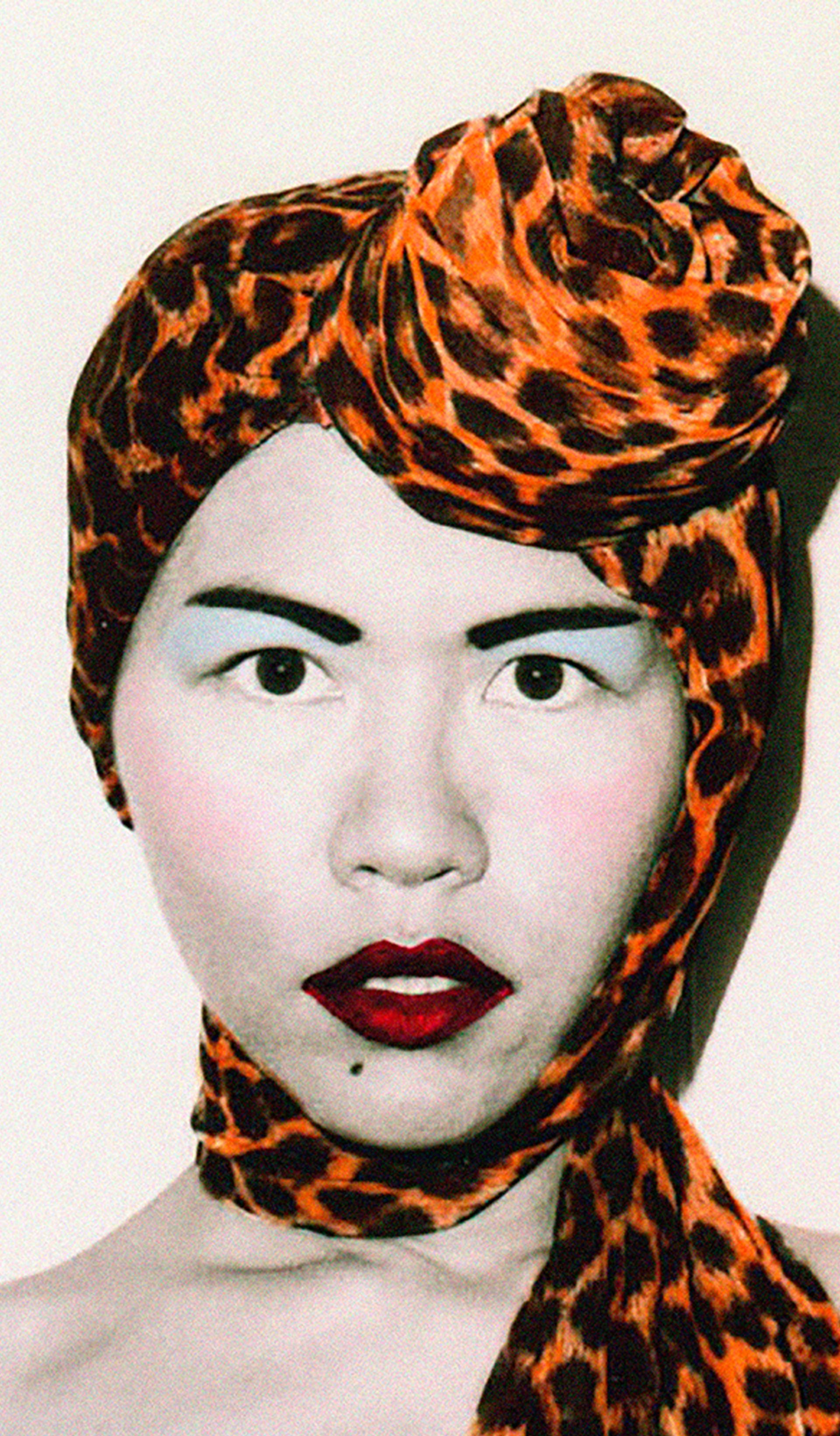 A photograph of fashion designers Jenny Lee and Linda Jackson. Both wear elaborate and highly colored headscarfs, along with a full face of carefully applied make-up.