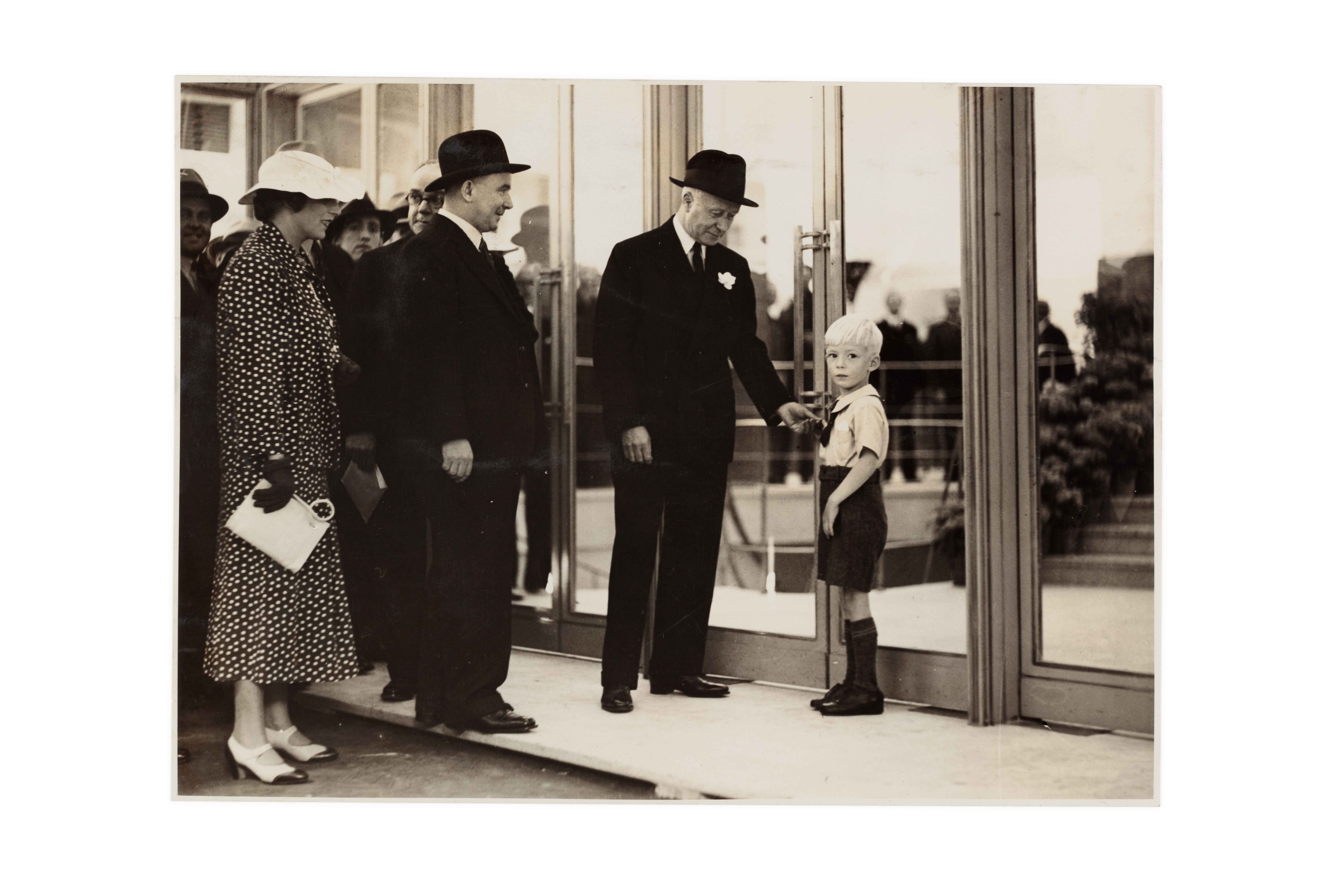 Two well-dressed men, a woman and a young boy outside closed department store doors.
