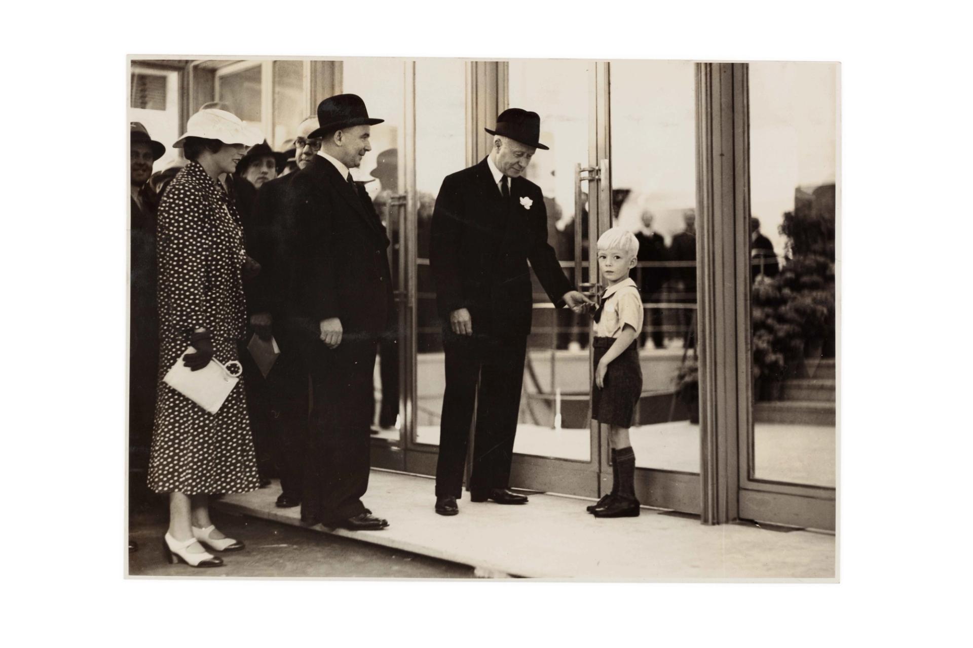 Two well-dressed men, a woman and a young boy outside closed department store doors.