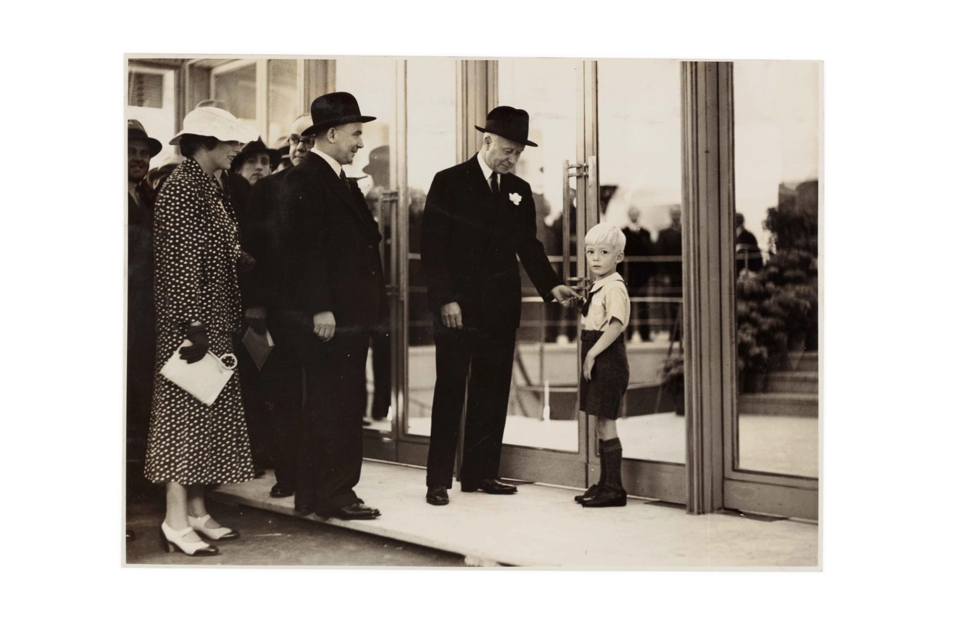 Two well-dressed men, a woman and a young boy outside closed department store doors.