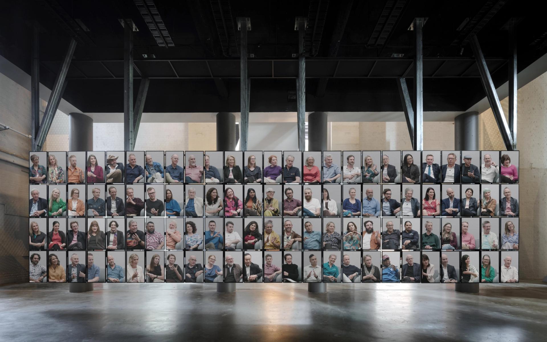 100 vertical screens with 100 people inside the screens, floating from the ceiling.