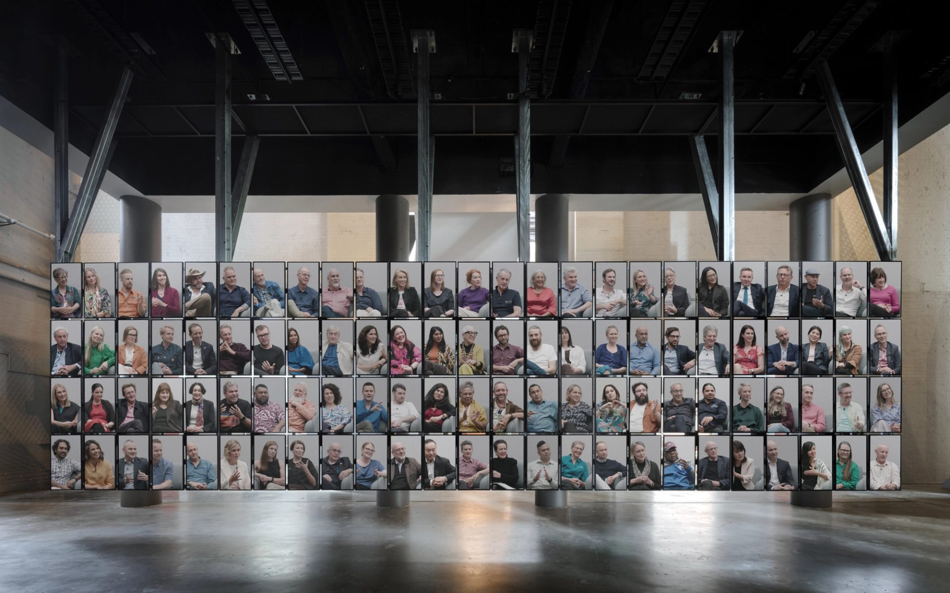 100 vertical screens with 100 people inside the screens, floating from the ceiling.