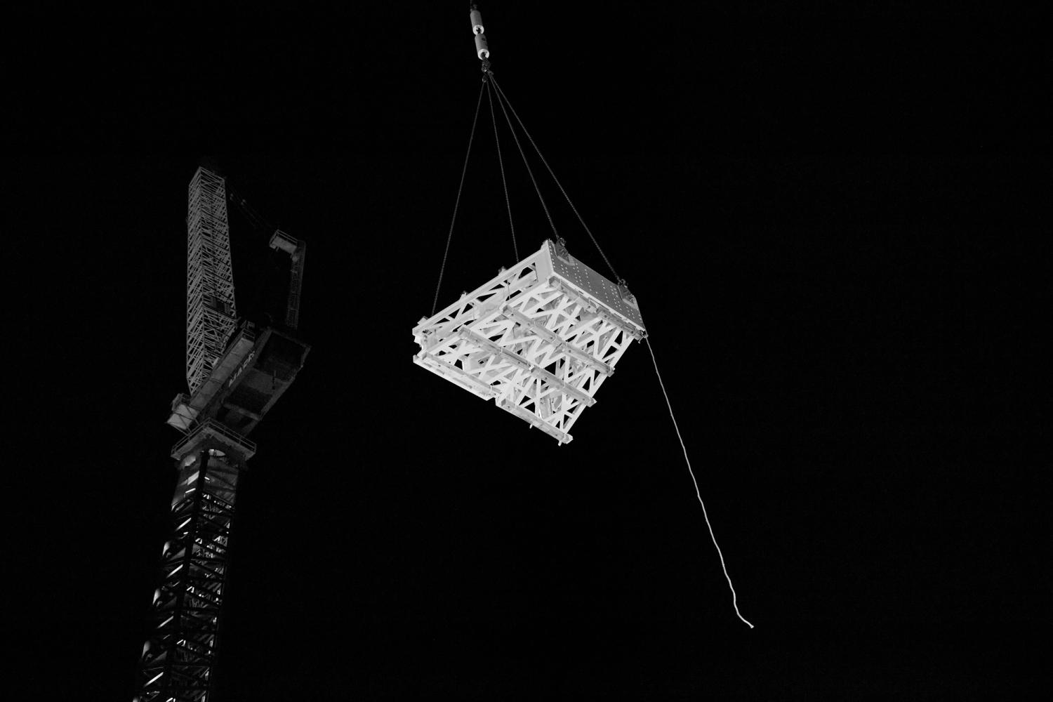 Singular geometric frame sits in the night sky held by a crane