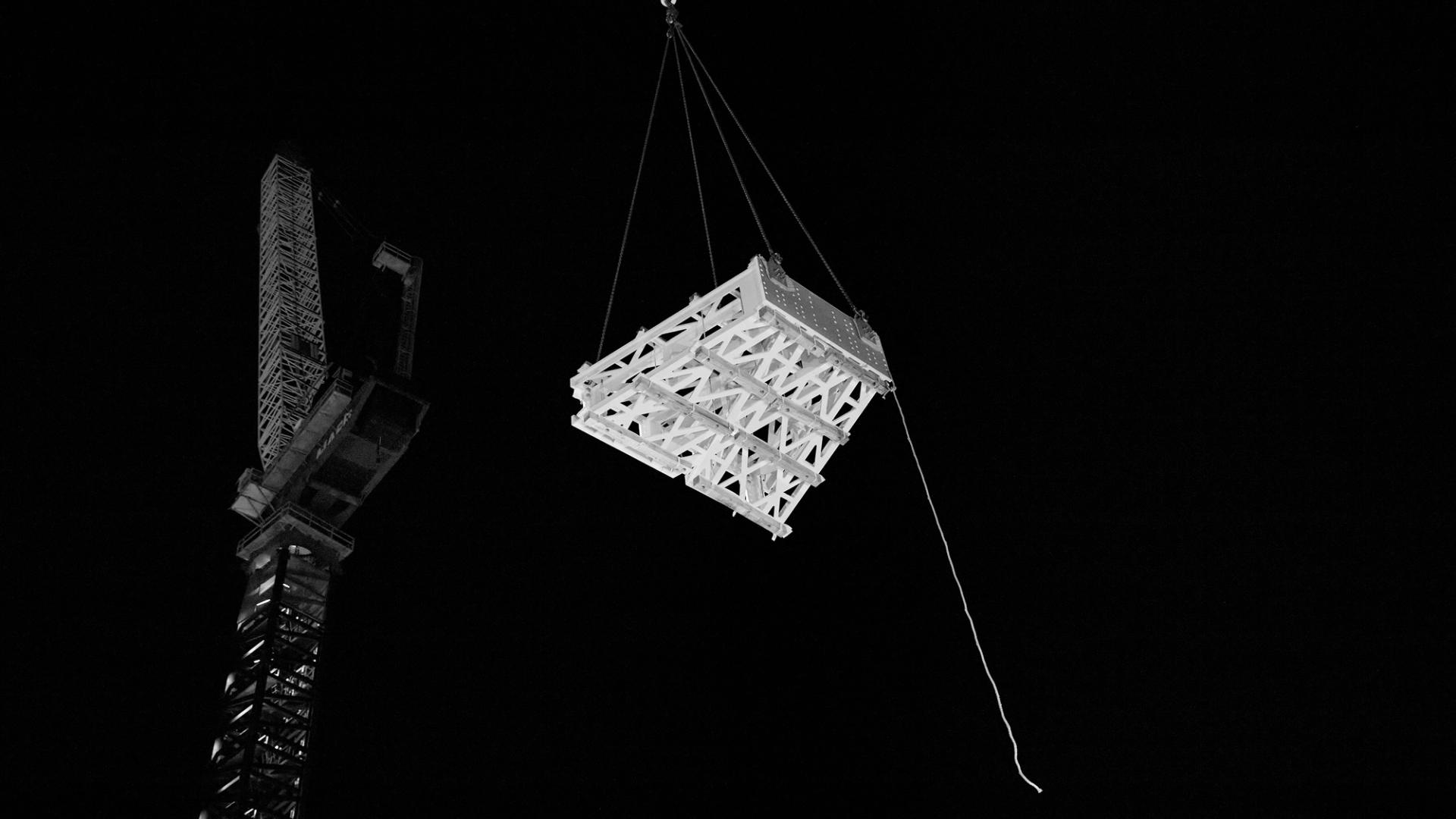 Singular geometric frame sits in the night sky held by a crane