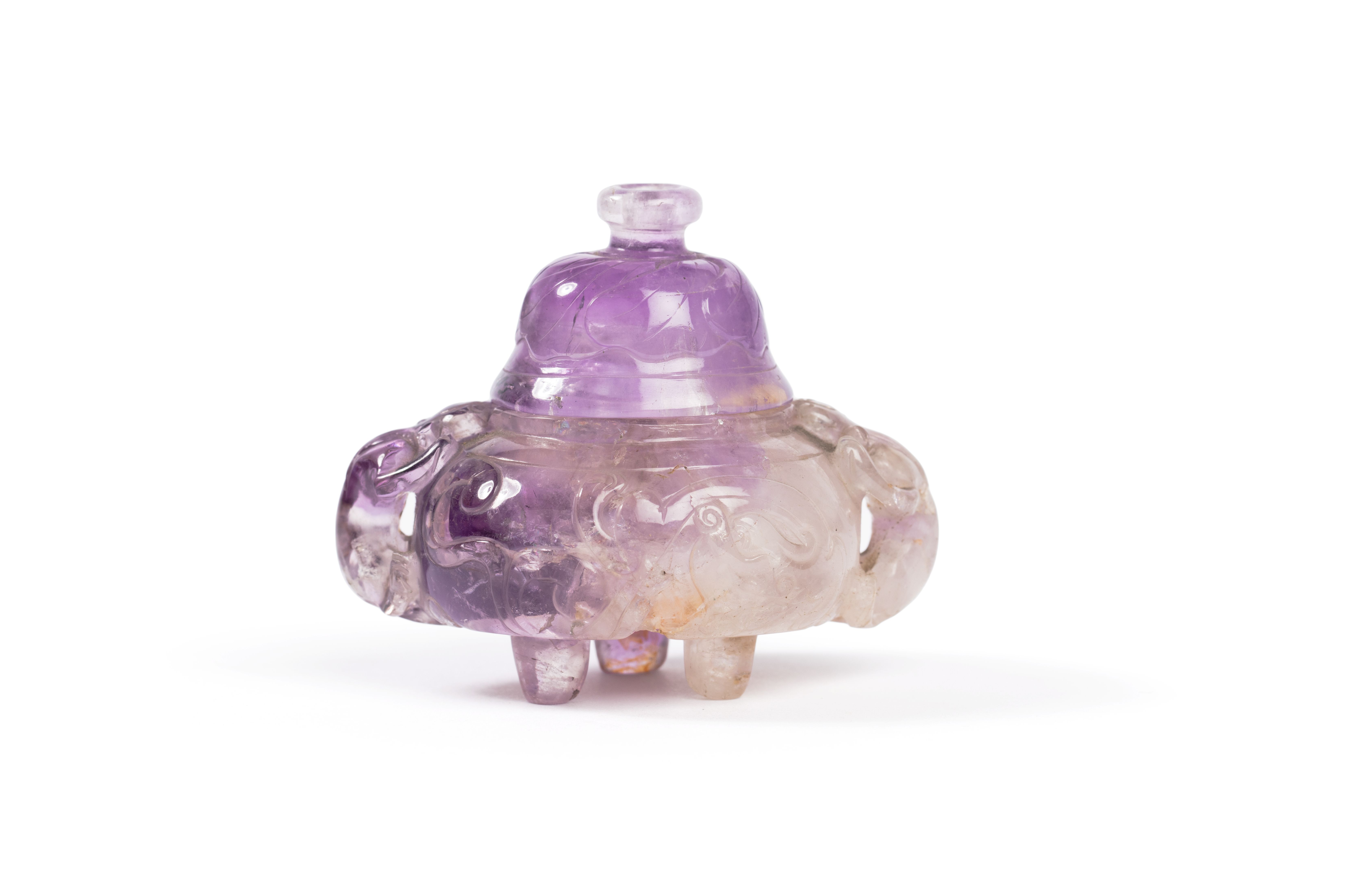 Censer with lid made of amethyst. The censer has a compressed globular shape with short straight tripod legs and two carved animal/lion shaped handles projecting from each side of the body. The flattened circular body has shallow relief carvings of dragon motifs around it. The high domed lid has a small circular upper knop that is shallow relief carved with floral motifs.