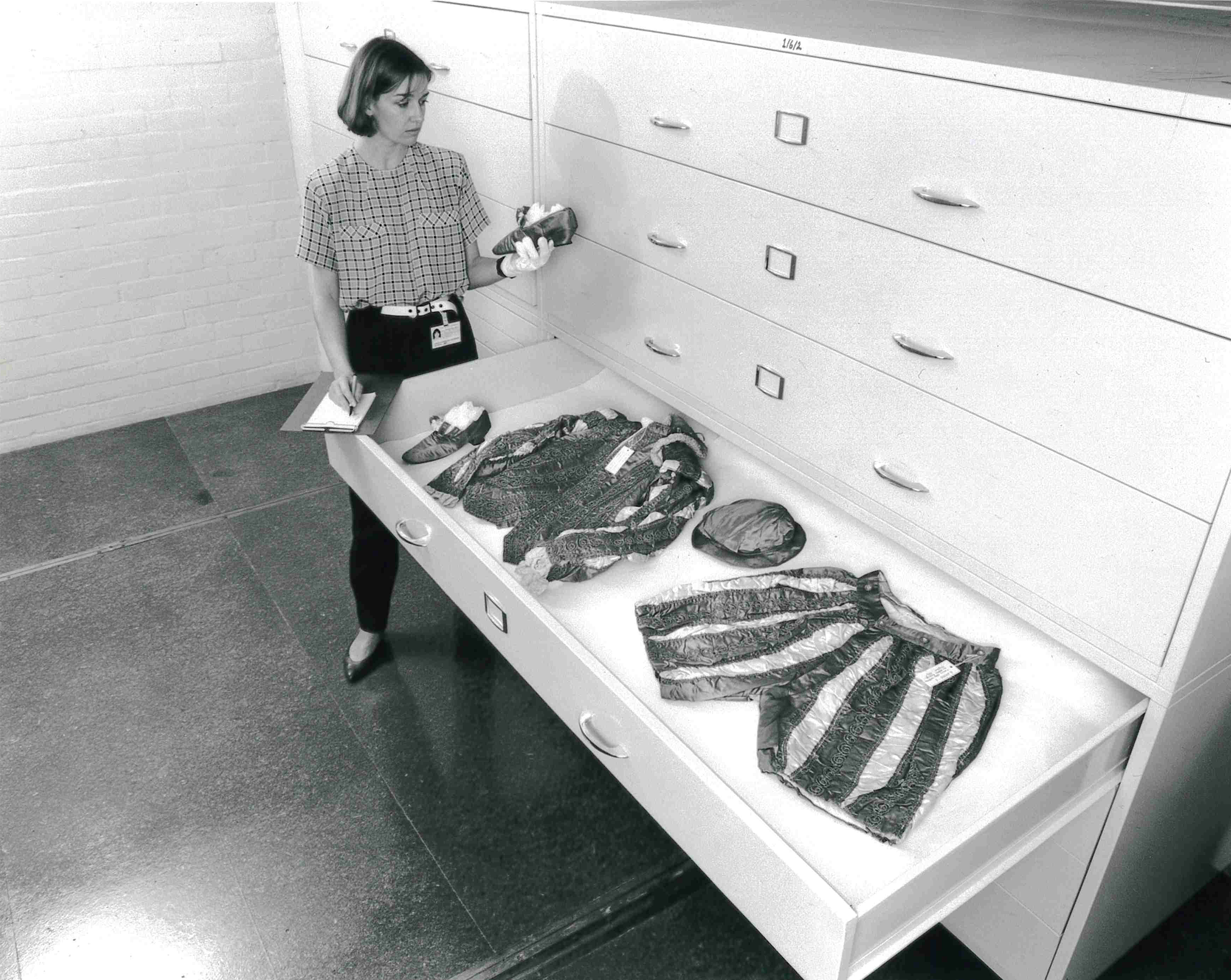 Black and white image of a museum employee opening storage drawers.