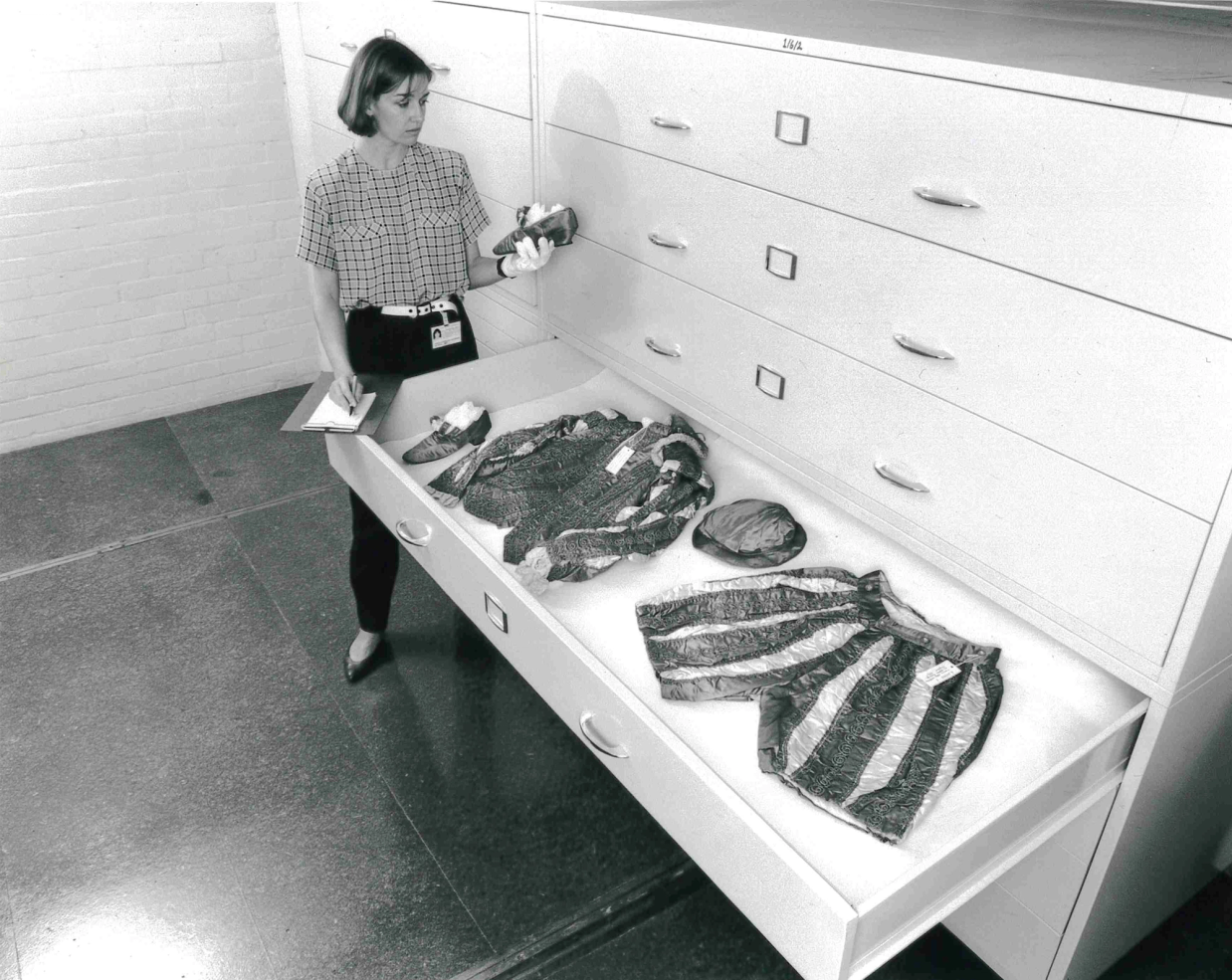 Black and white image of a museum employee opening storage drawers