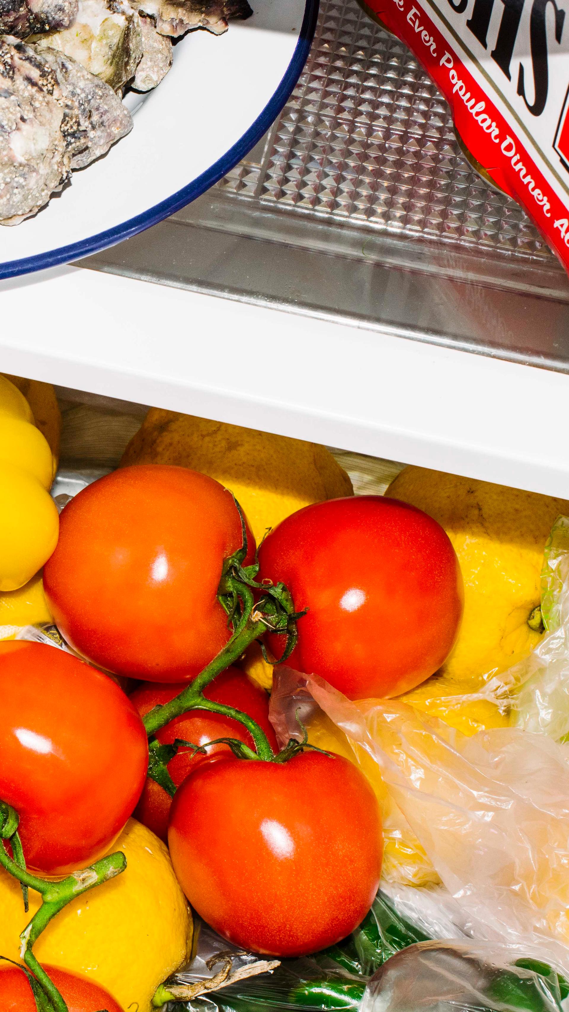 The vegetable drawer of a fridge is slightly open. The drawer is full of red and yellow tomatoes.